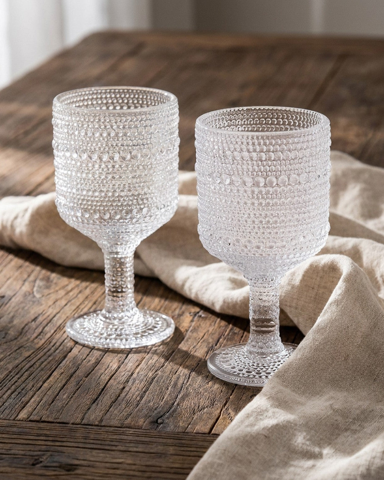 Two textured glass goblets on a wooden surface with a beige cloth.