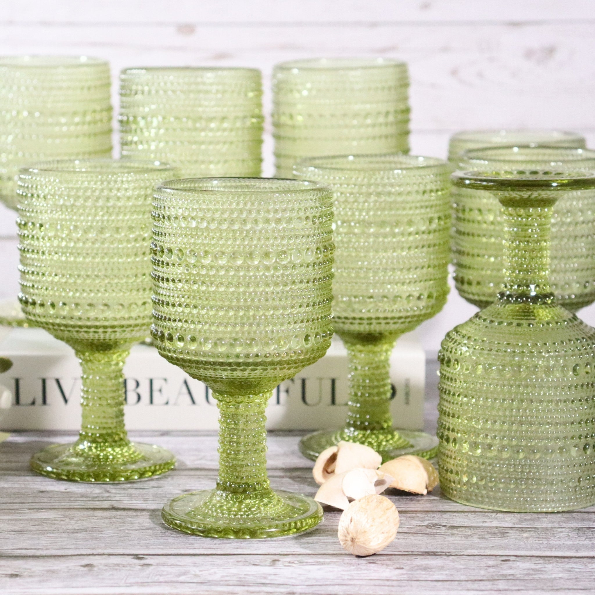 Set of green textured glass goblets on a wooden surface with a white background