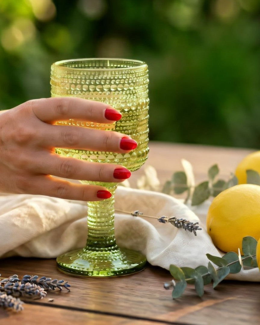 Two green textured glass goblets on a wooden surface with decorative elements.