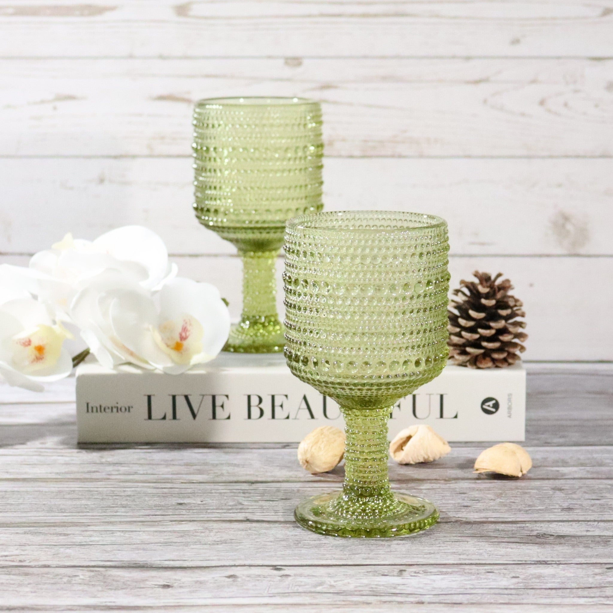 Two green textured glass goblets on a wooden surface with decorative elements.