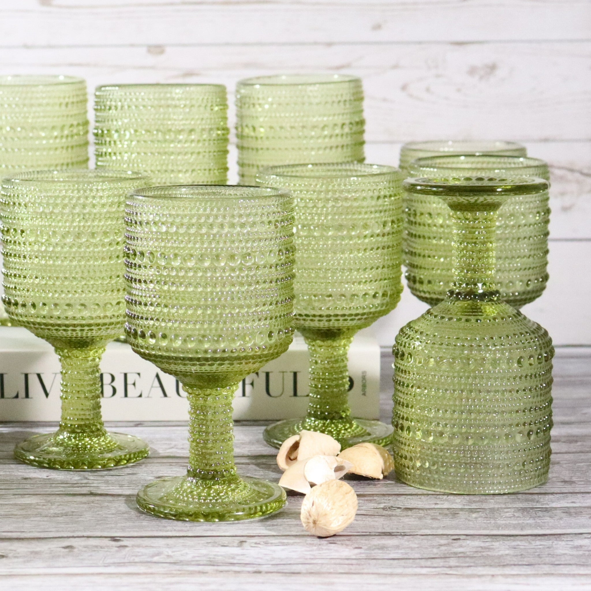 Set of green textured glass goblets on a wooden surface with a blurred book in the background.