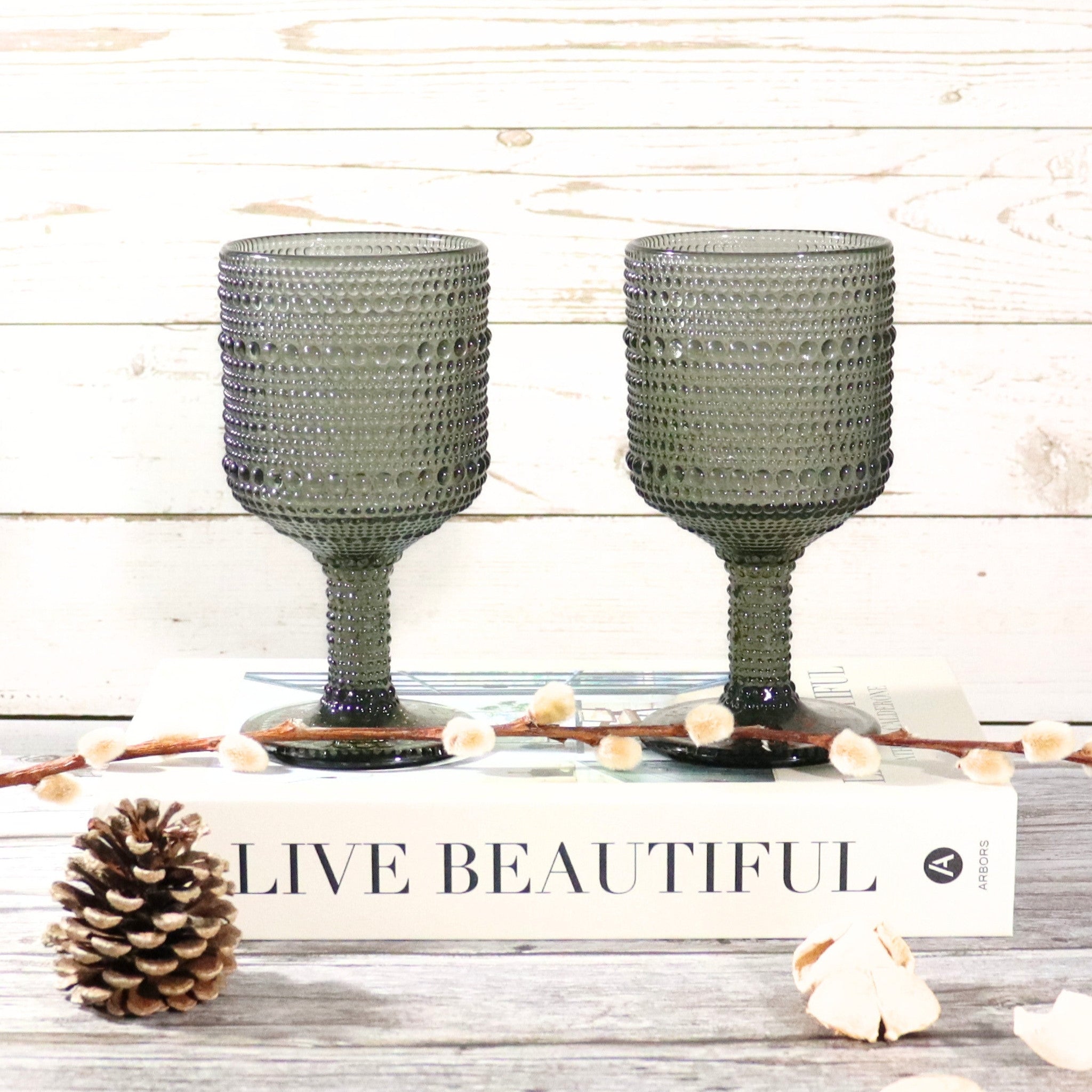 Two gray textured glass goblets on a wooden surface with decorative elements.