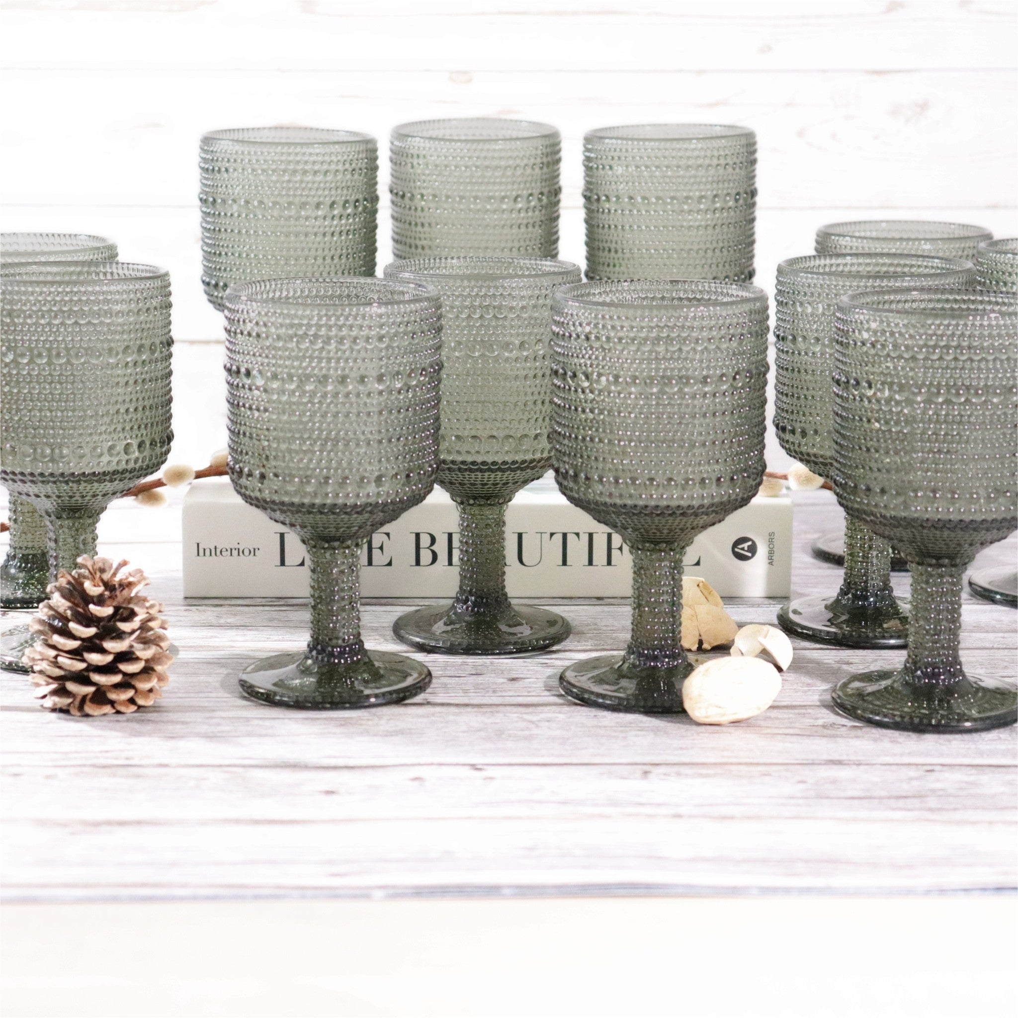 Set of textured gray glass goblets on a wooden surface with decorative items.