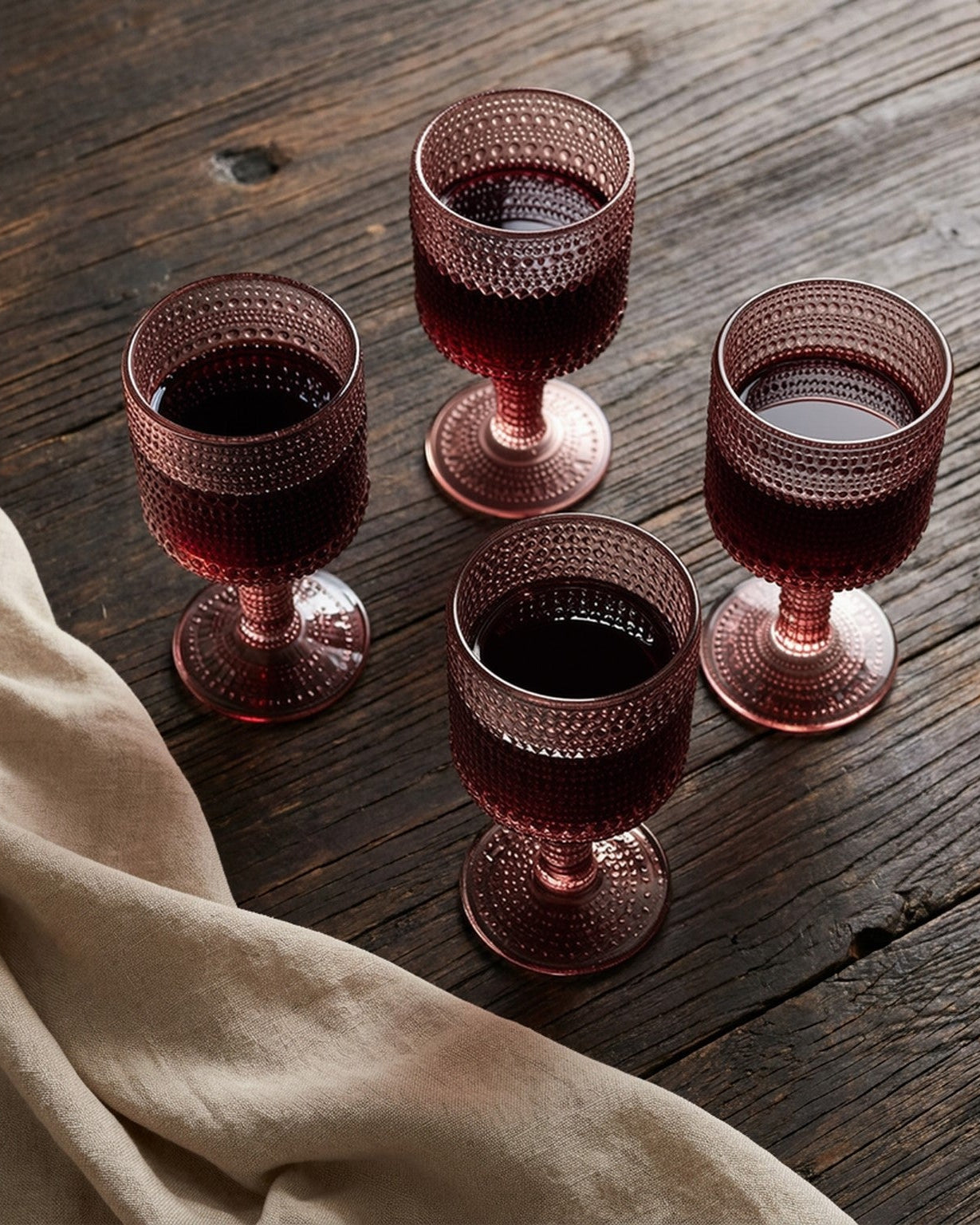 Set of four pink textured glass goblets on a decorative table with greenery and 'This is Home' sign.