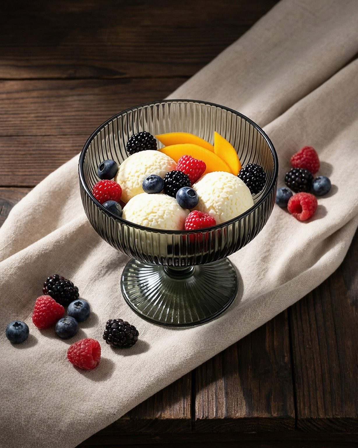 Dark grey glass bowl with ice cream and fruit on a wooden surface