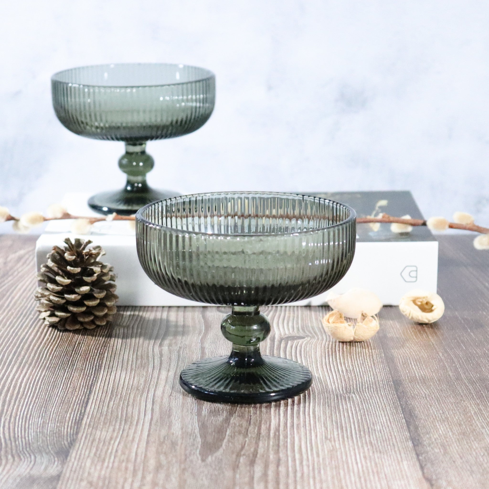Two grey glass fruit bowls on a wooden surface with decorative elements.