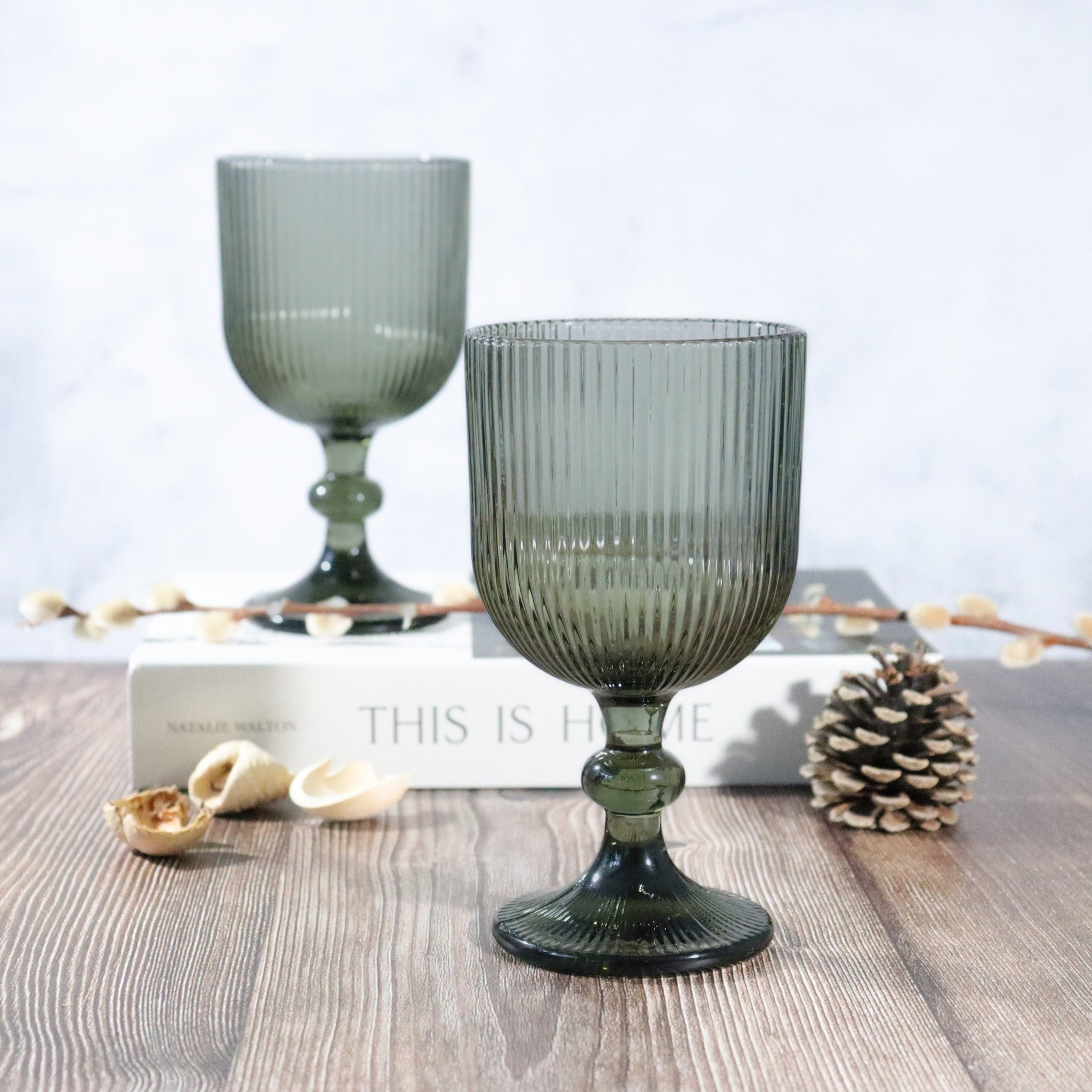 Two ribbed green glass goblets on a wooden surface with decorative elements.
