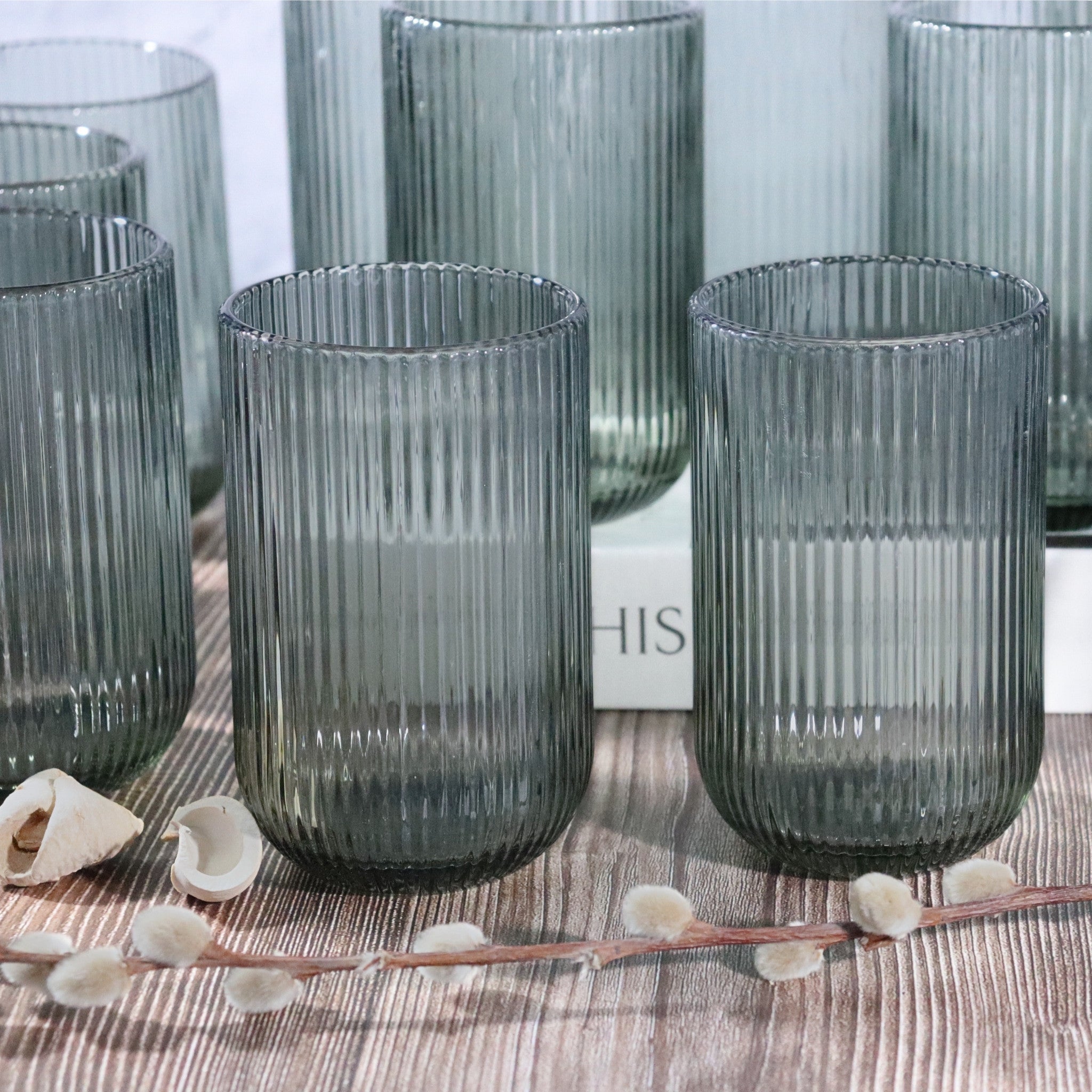 Set of ribbed glass tumblers on a wooden surface with seashells and branches.