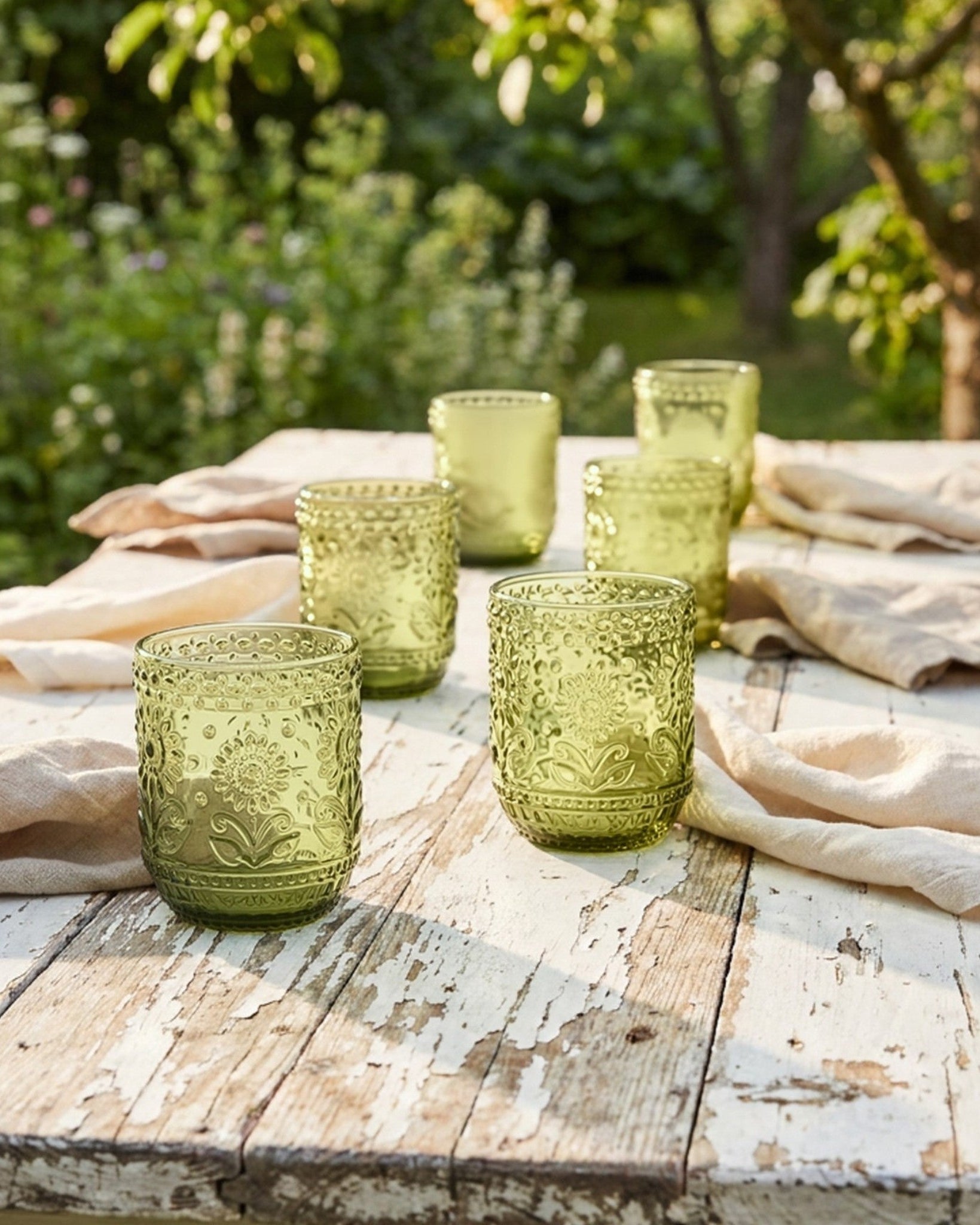 Green glass tumblers on a wooden table outdoors with a natural background