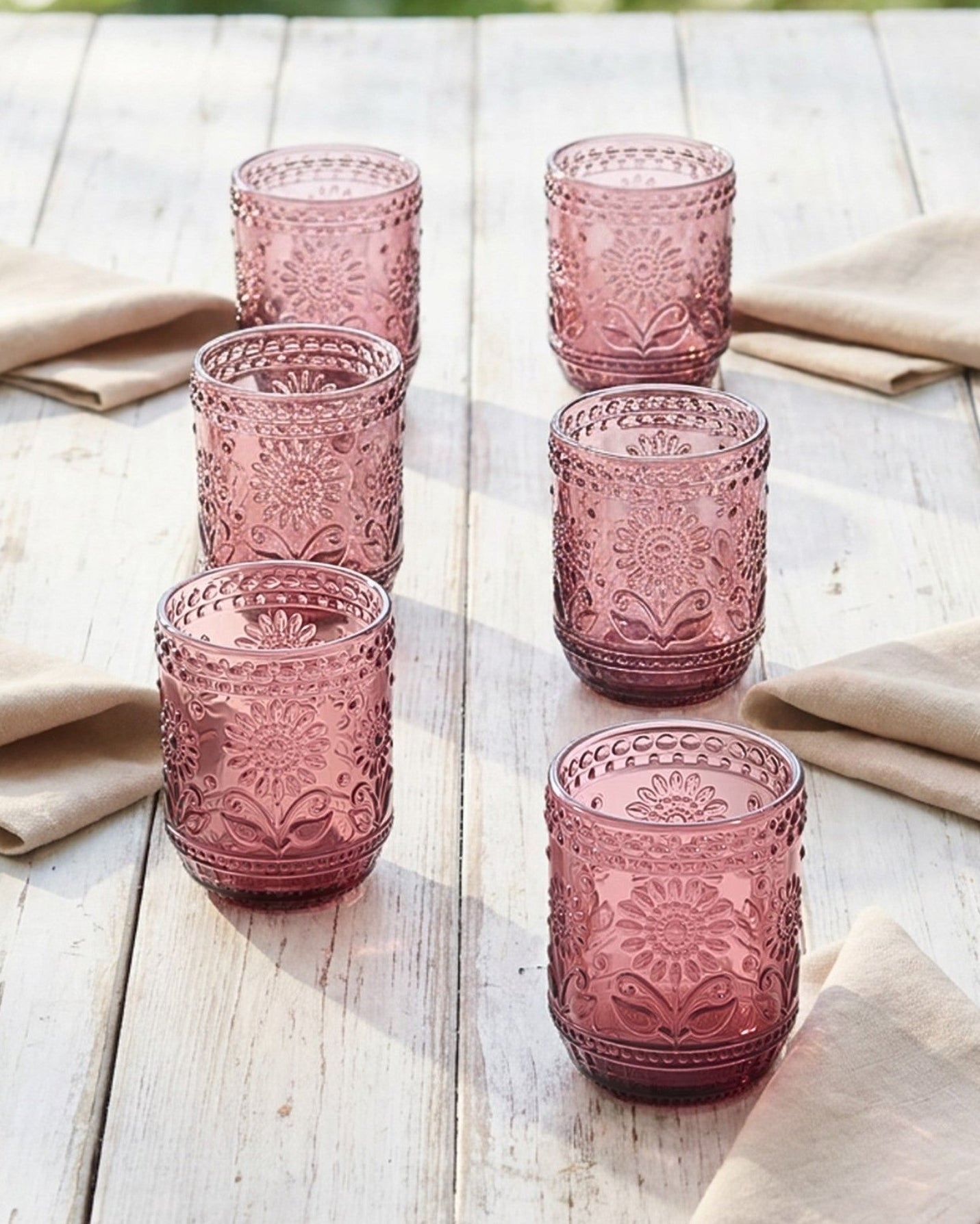 Set of pink glass tumblers on a wooden table with beige napkins.