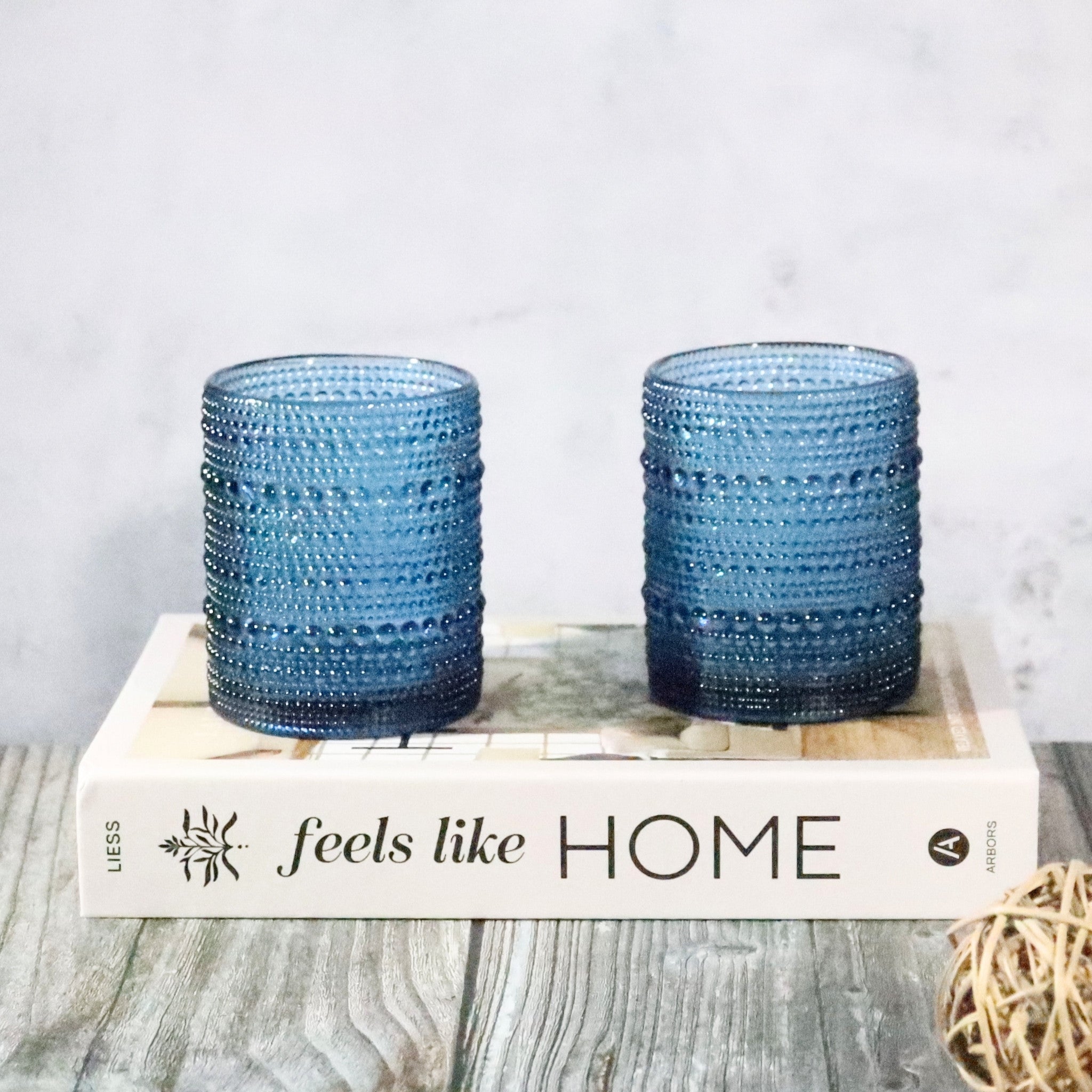 Two blue textured glass tumblers on a book titled 'feels like HOME'.
