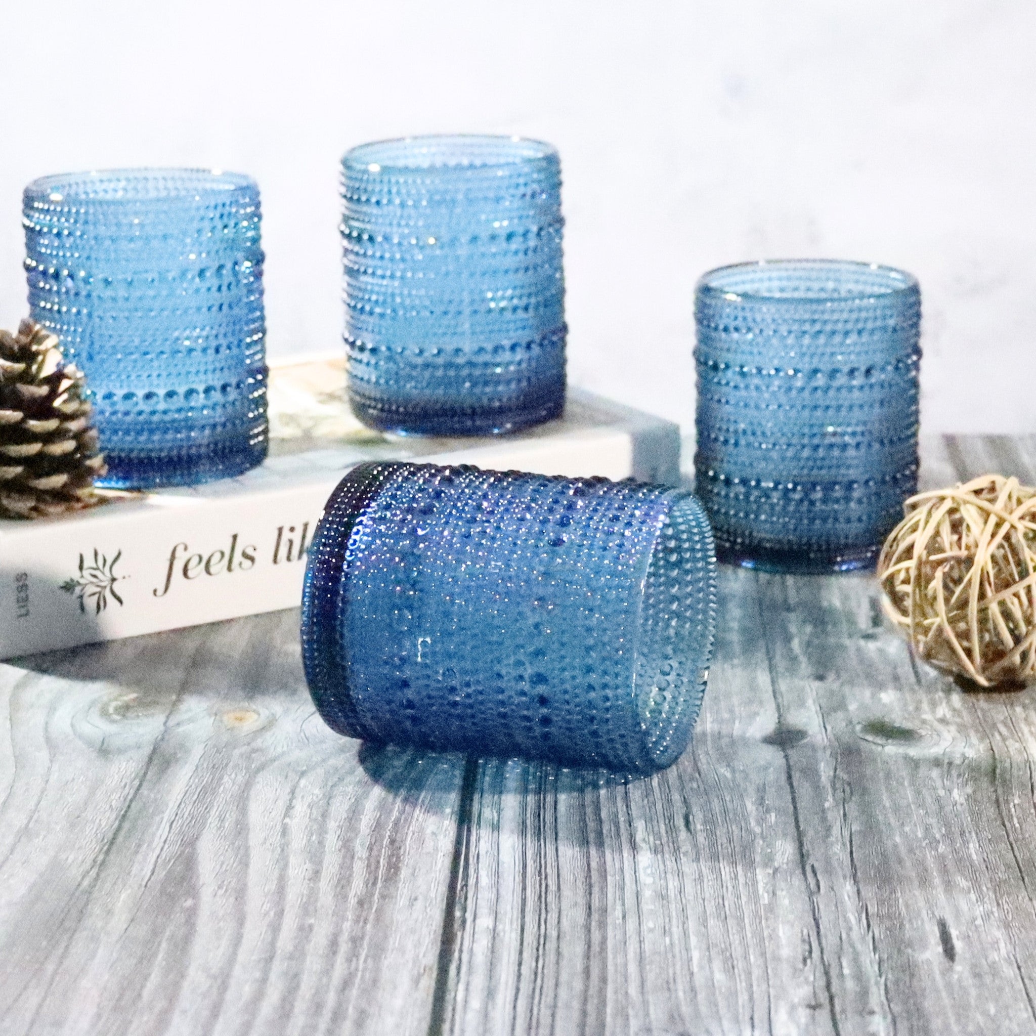 Set of blue textured glass tumblers on a wooden surface with decorative elements.