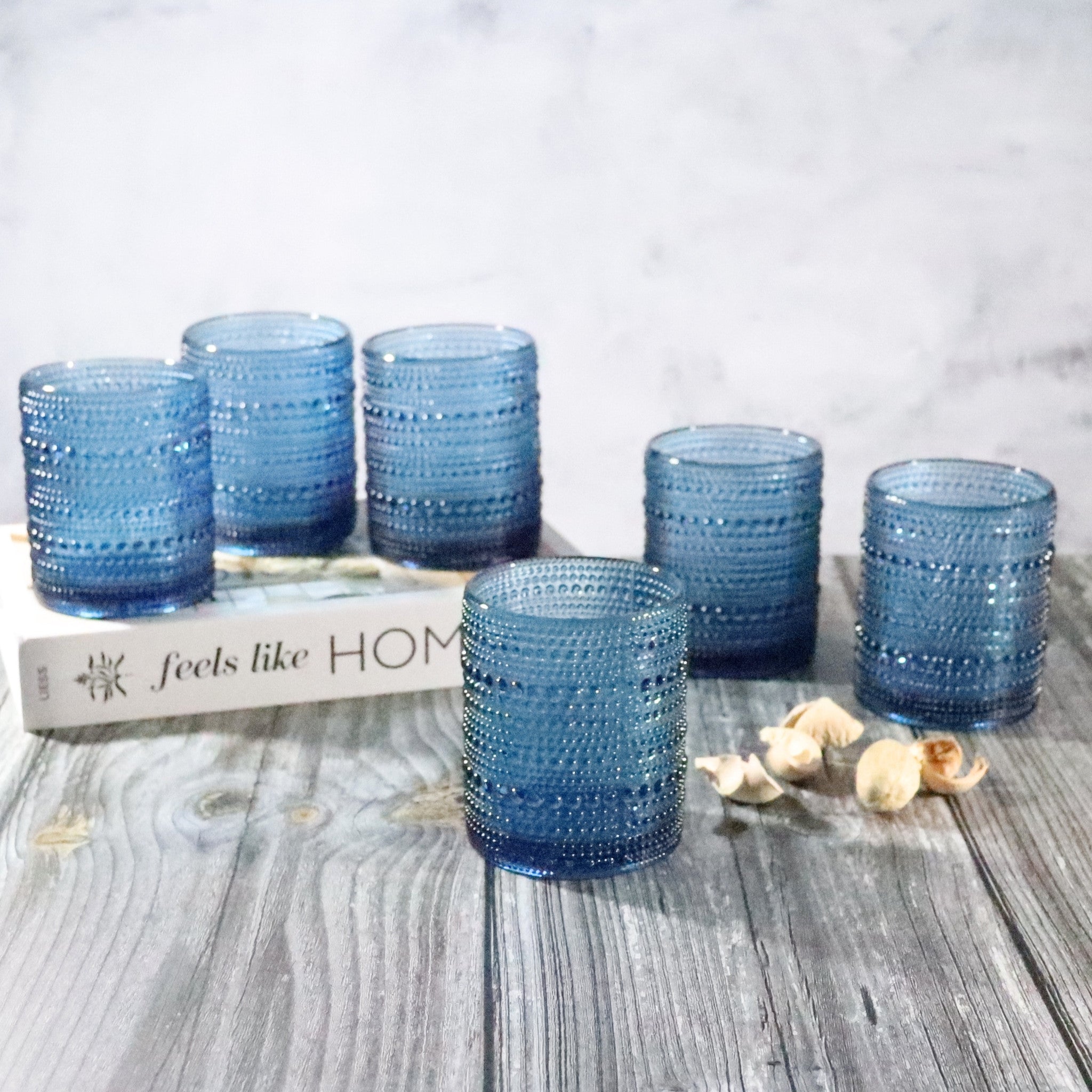 Set of blue textured glass tumblers on a wooden surface with a 'feels like home' book.