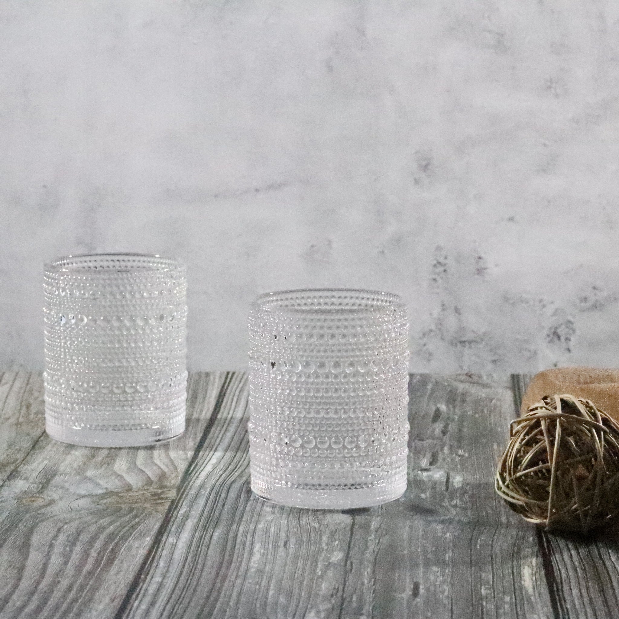 Two textured beaded hobnail old fashioned tumblers on a wooden surface with a marble background