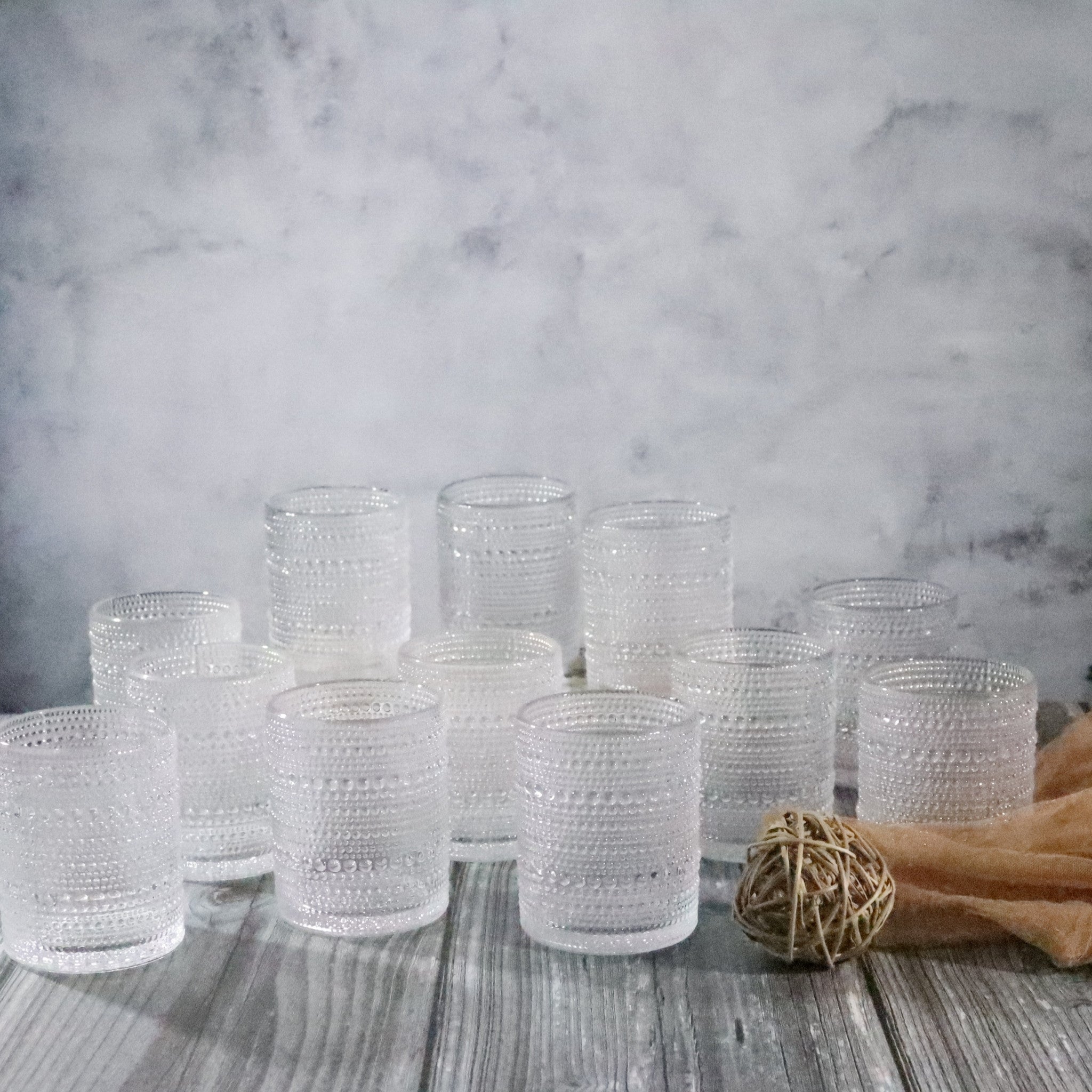 Set of 12 clear hobnail glass tumblers on a wooden surface with a marble background