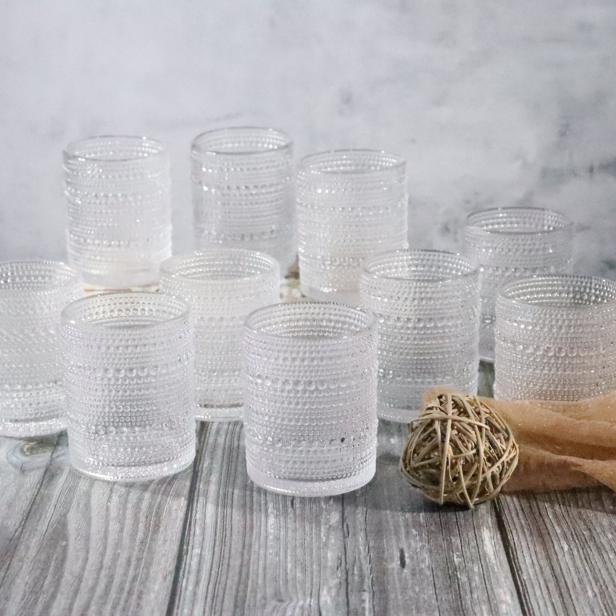 Set of beaded hobnail old fashioned rocks tumblers on a wooden surface with a light gray background