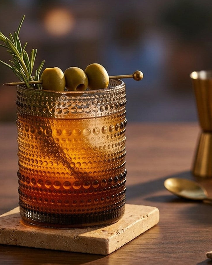 Set of grey textured glass tumblers on a wooden surface with a pine cone.