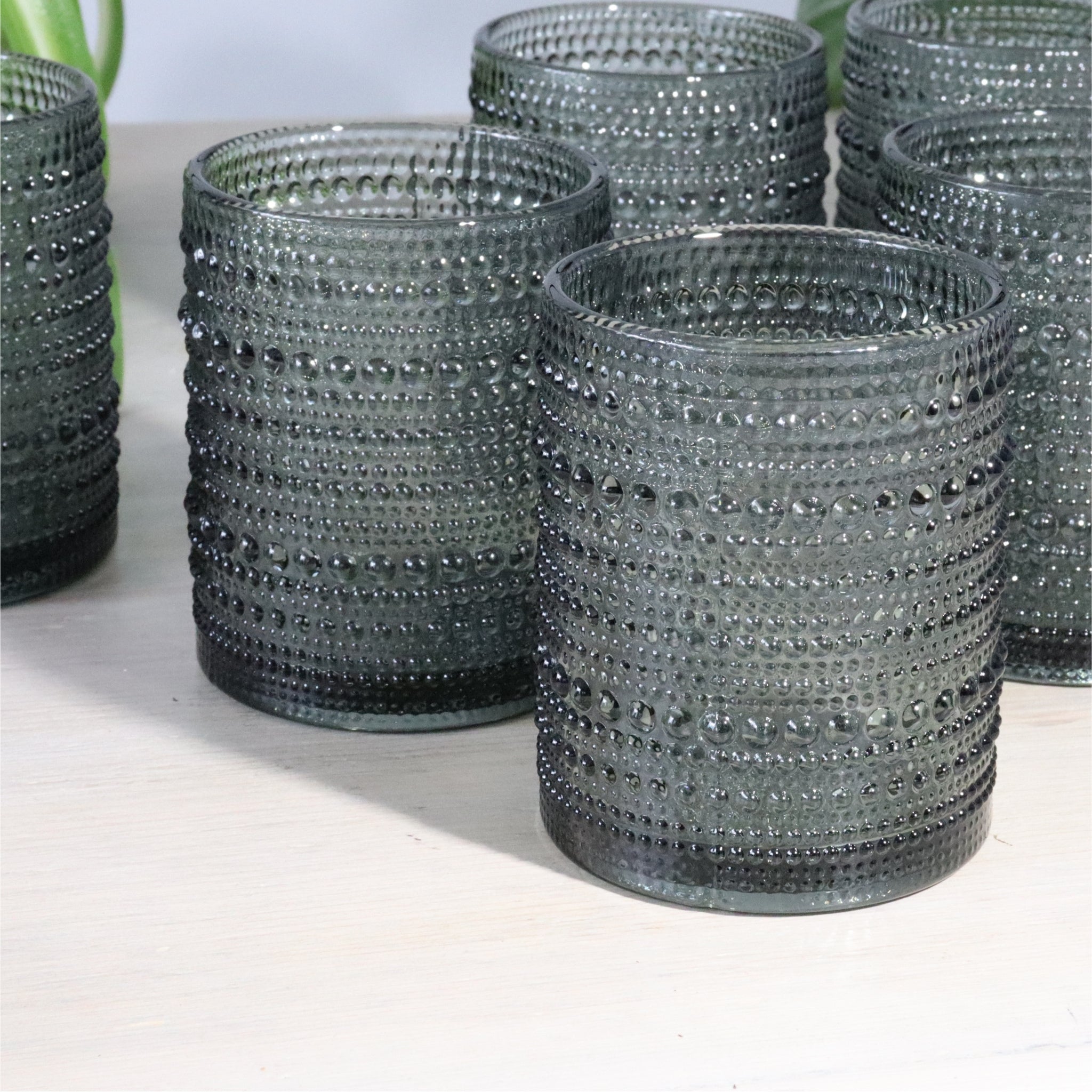 Four hobnail gray glass tumblers on a wooden surface with a blurred green background