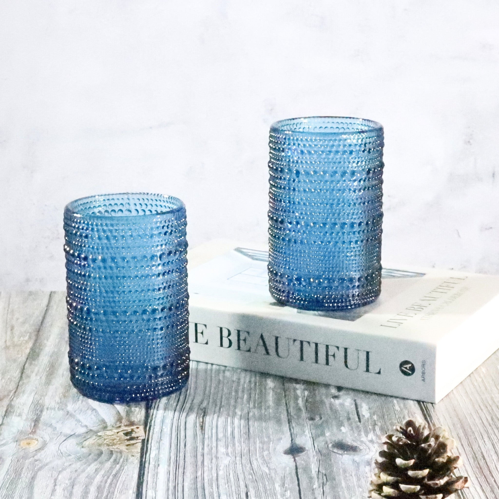 Two blue textured glass vases on a wooden surface with a book underneath.
