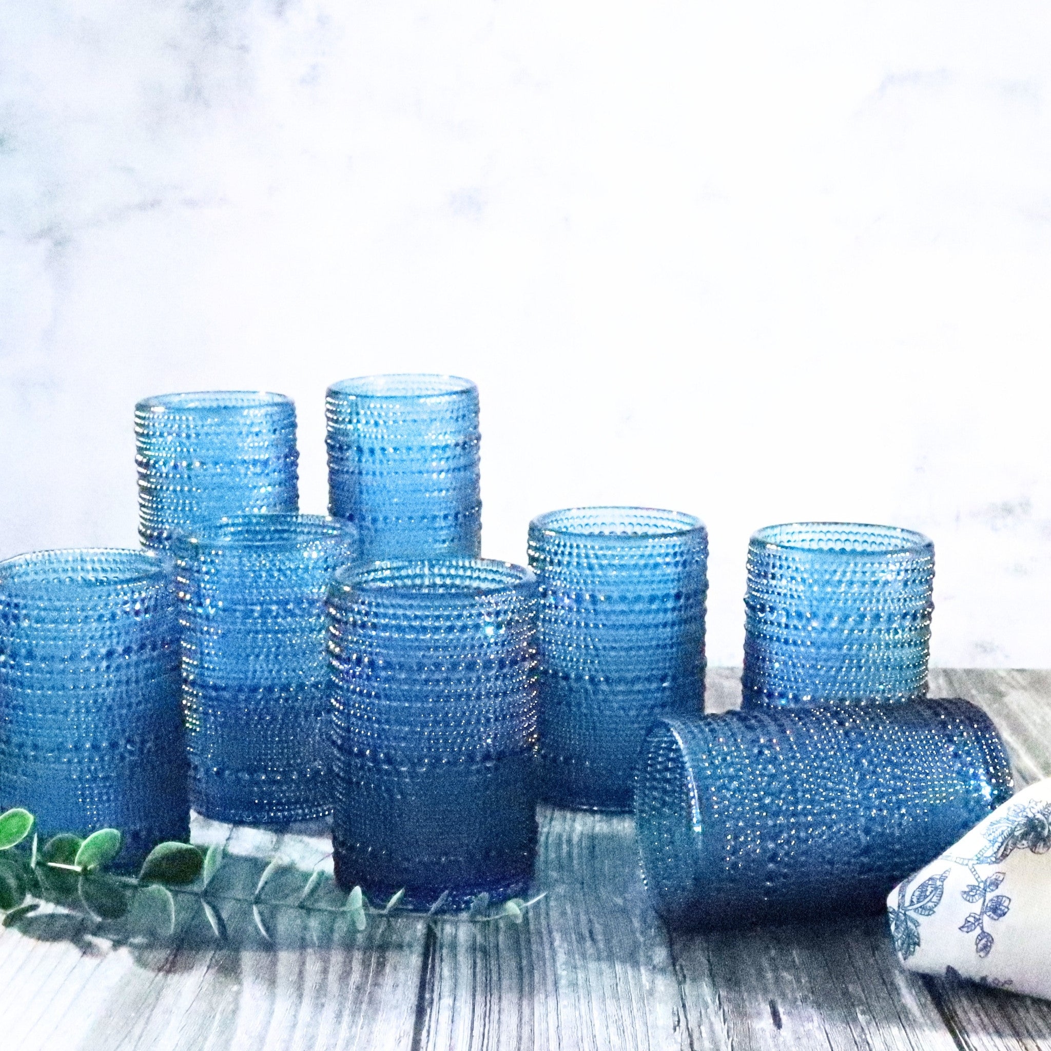Set of blue textured glass tumblers on a wooden surface with a white background