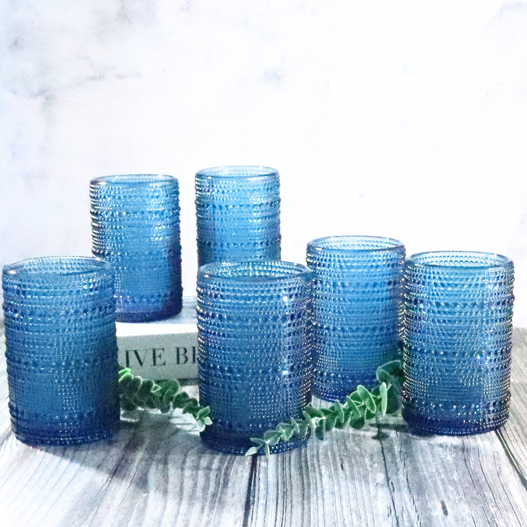 Set of blue textured glass tumblers on a light wooden surface with a white background