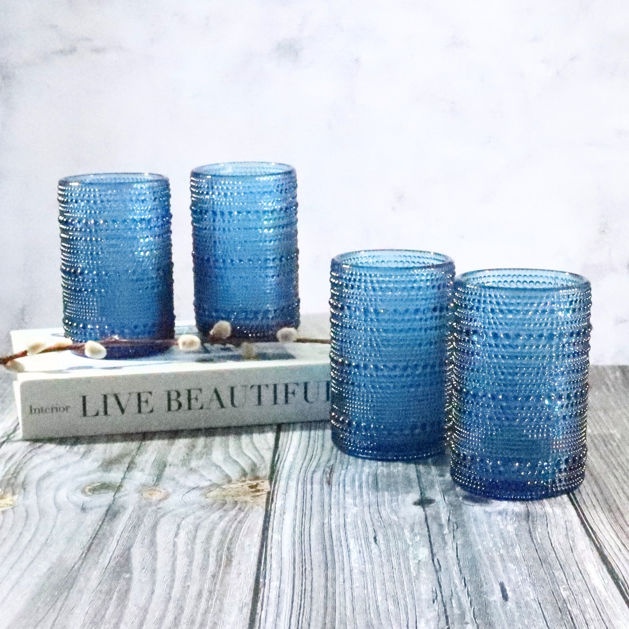 Set of four blue textured glass tumblers on a wooden surface with a book in the background.
