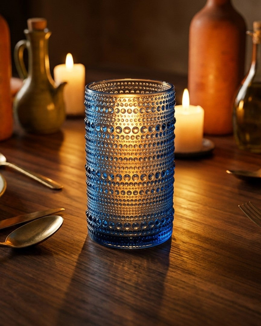 Set of four blue textured glass tumblers on a wooden surface with a book in the background.