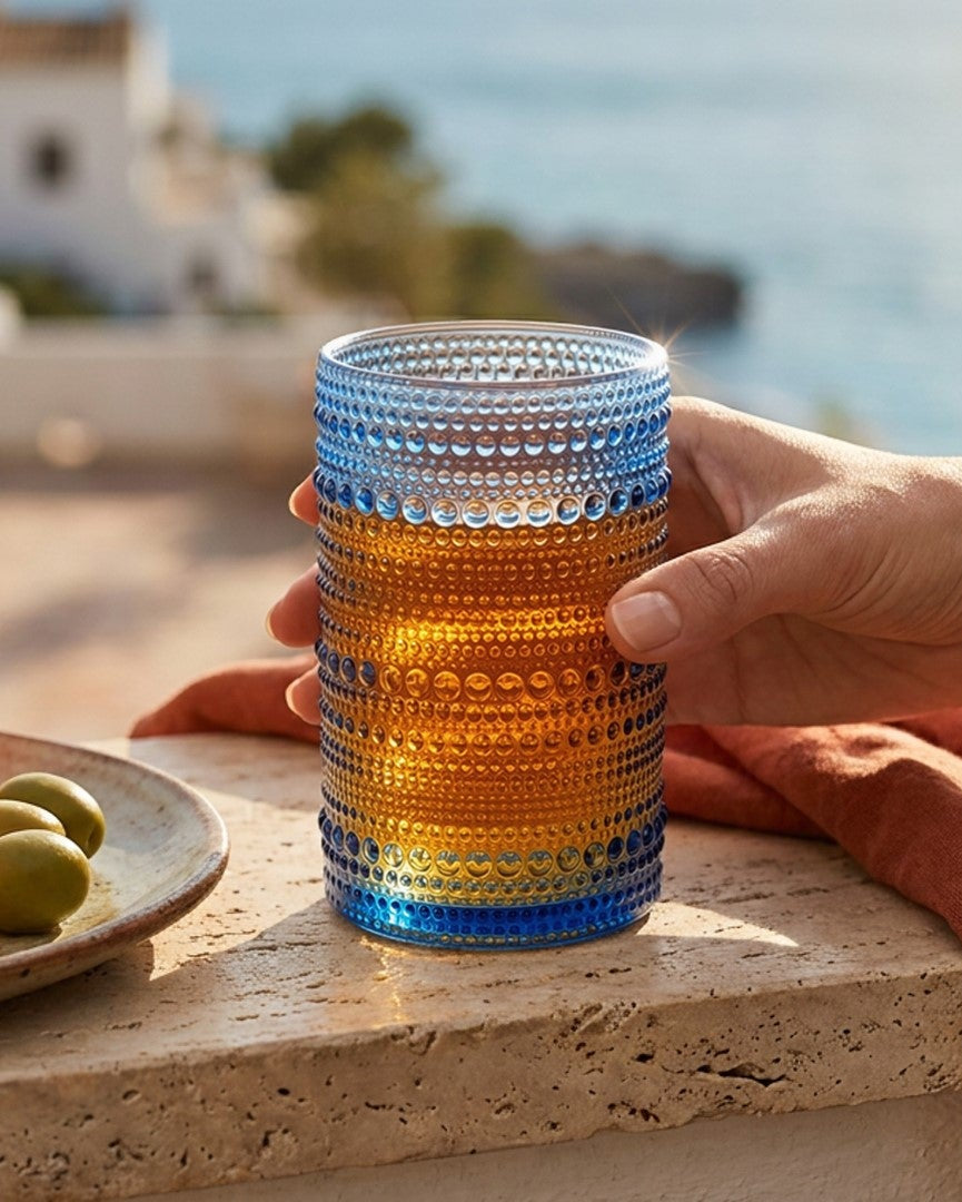 Set of four blue textured glass tumblers on a wooden surface with a 'Live Beautiful' book in the background.