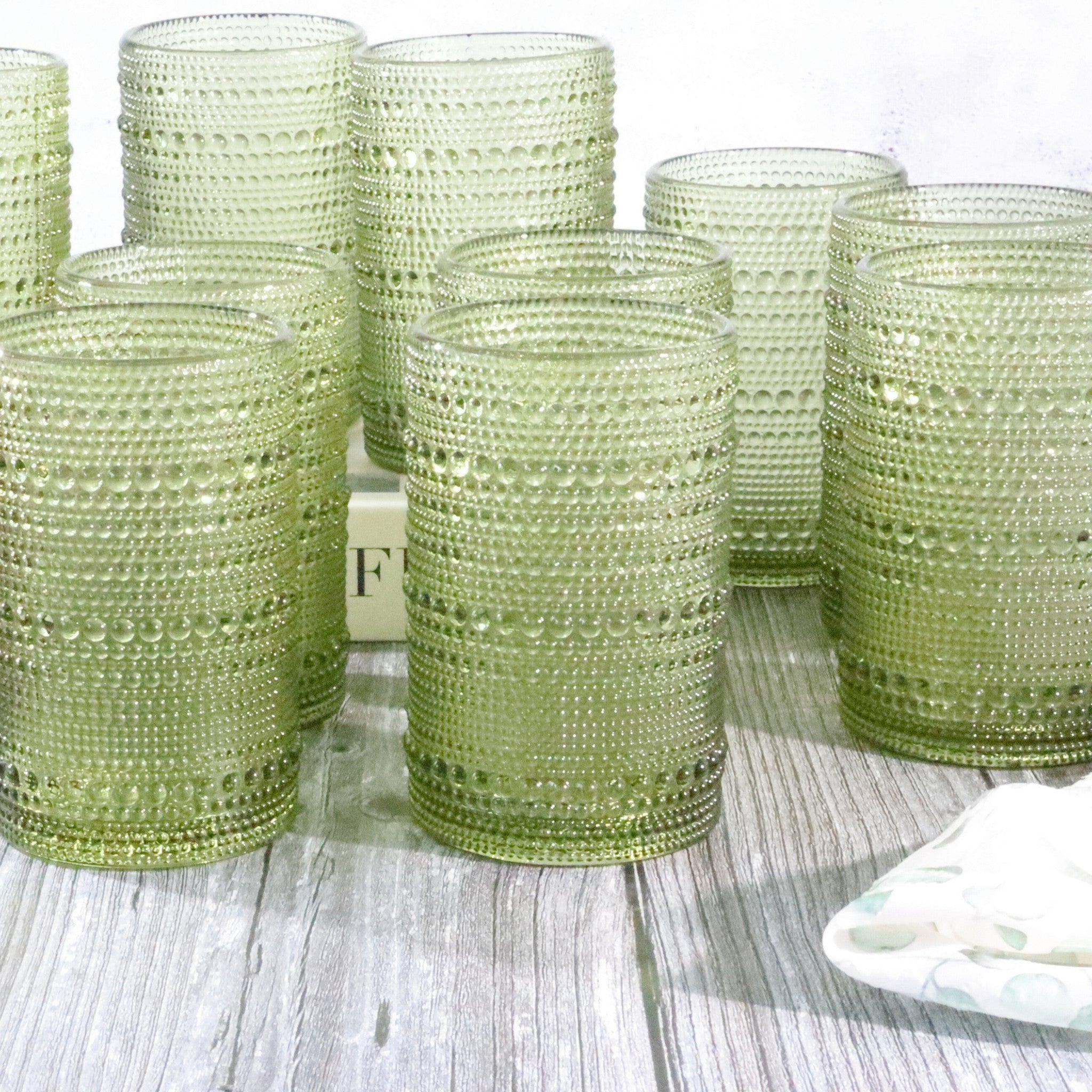Set of green hobnail bead glass tumblers on a wooden surface