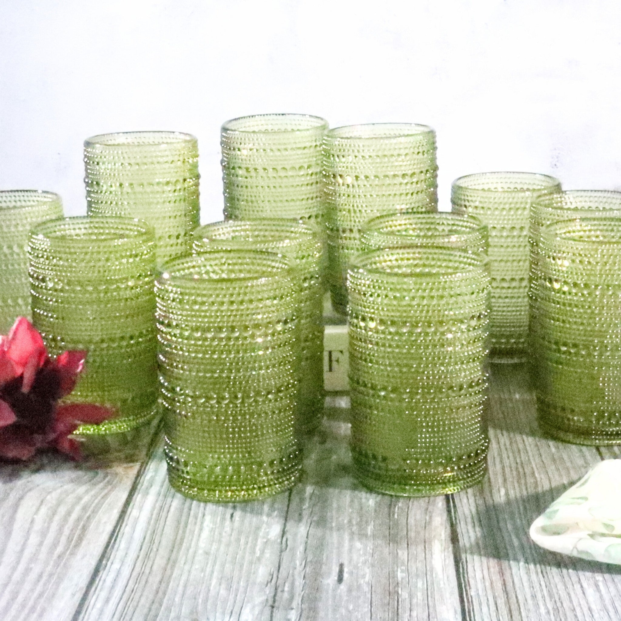 Set of green beaded tumblers on a wooden surface with a white background