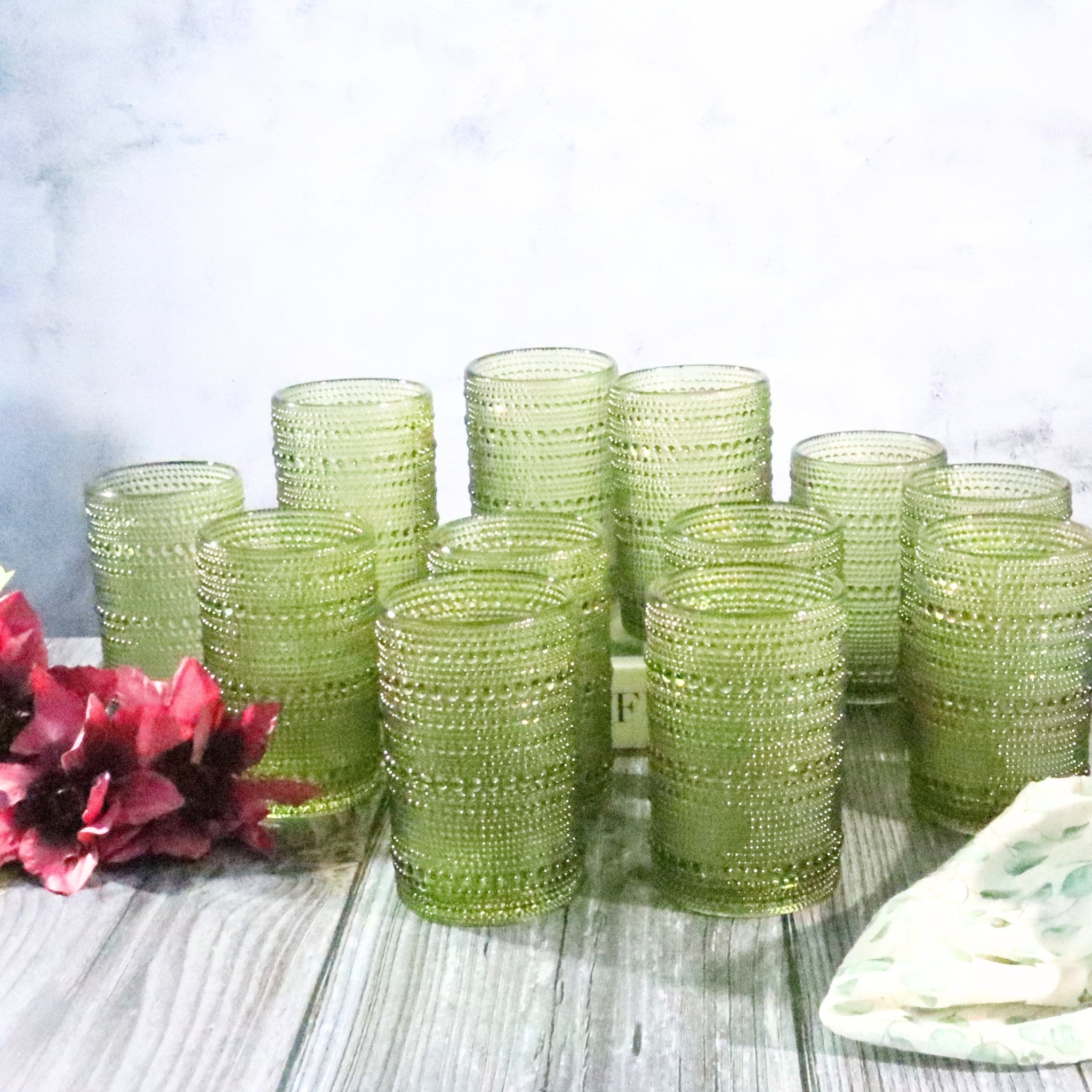Set of green beaded tumblers on a wooden surface with flowers and a plate.