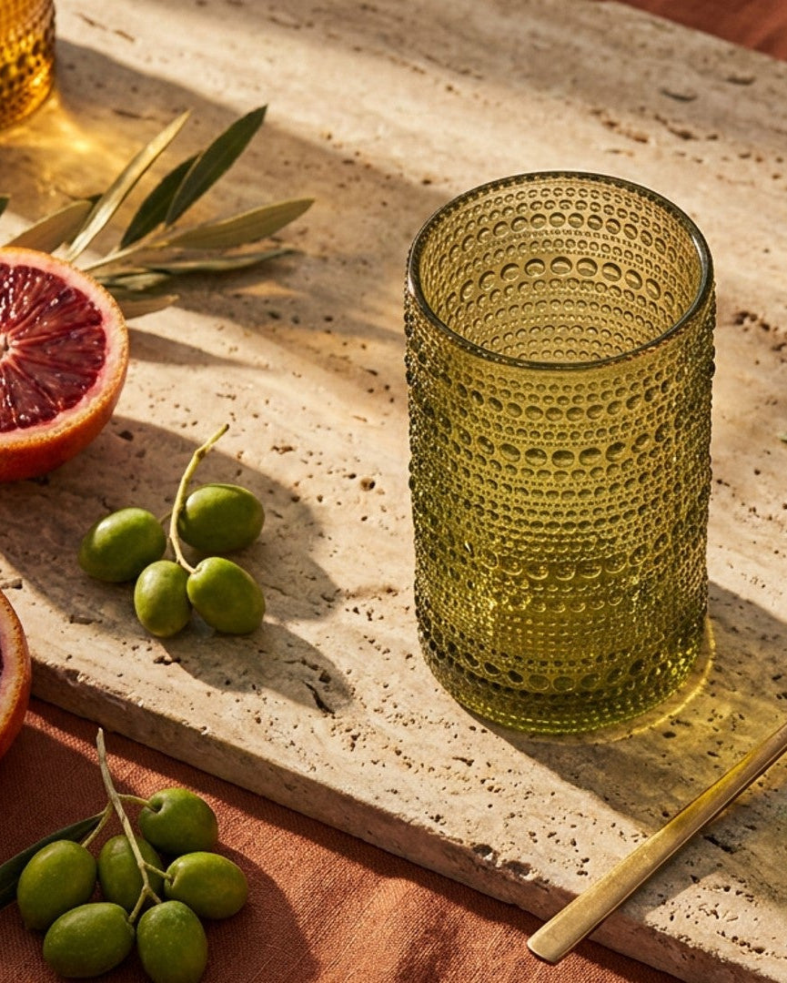 Set of green textured glass tumblers on a wooden surface with a book and pink flower in the background.