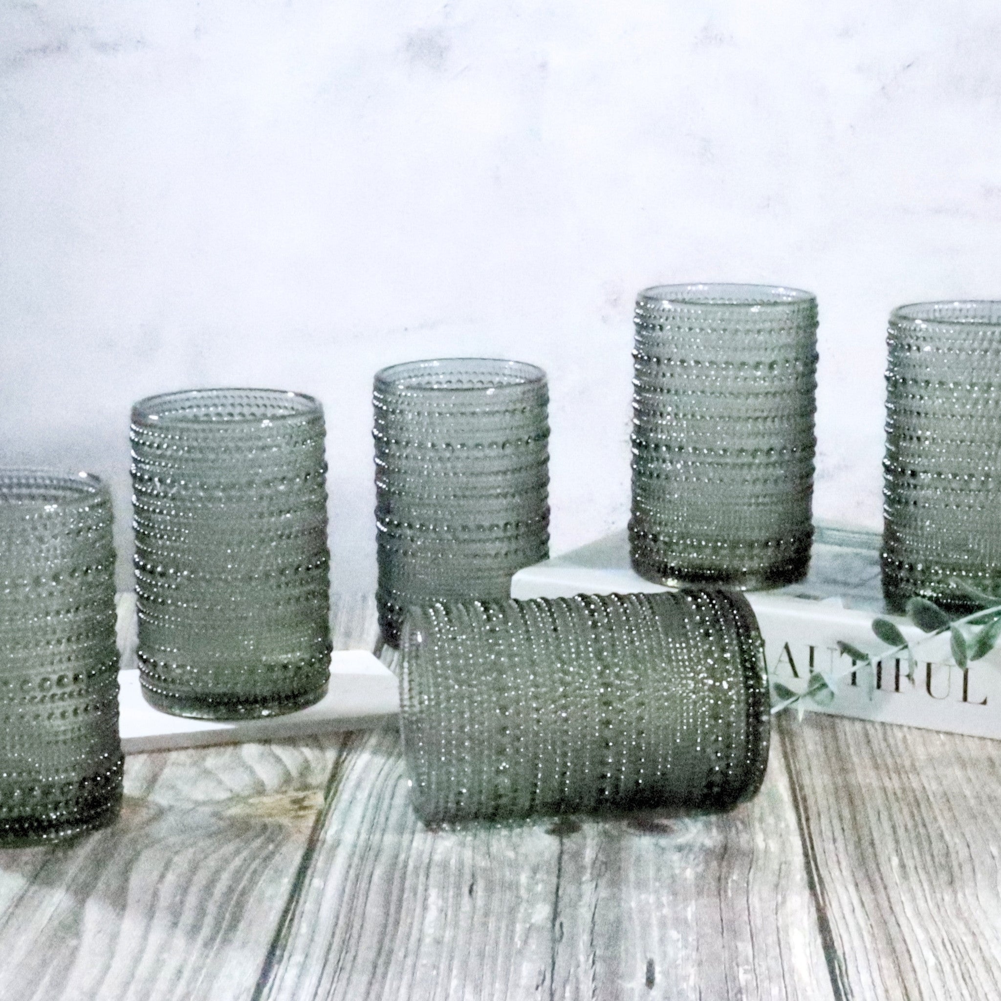 Set grey coloured hobnail beaded glass tumblers on a wooden surface with a blurred background