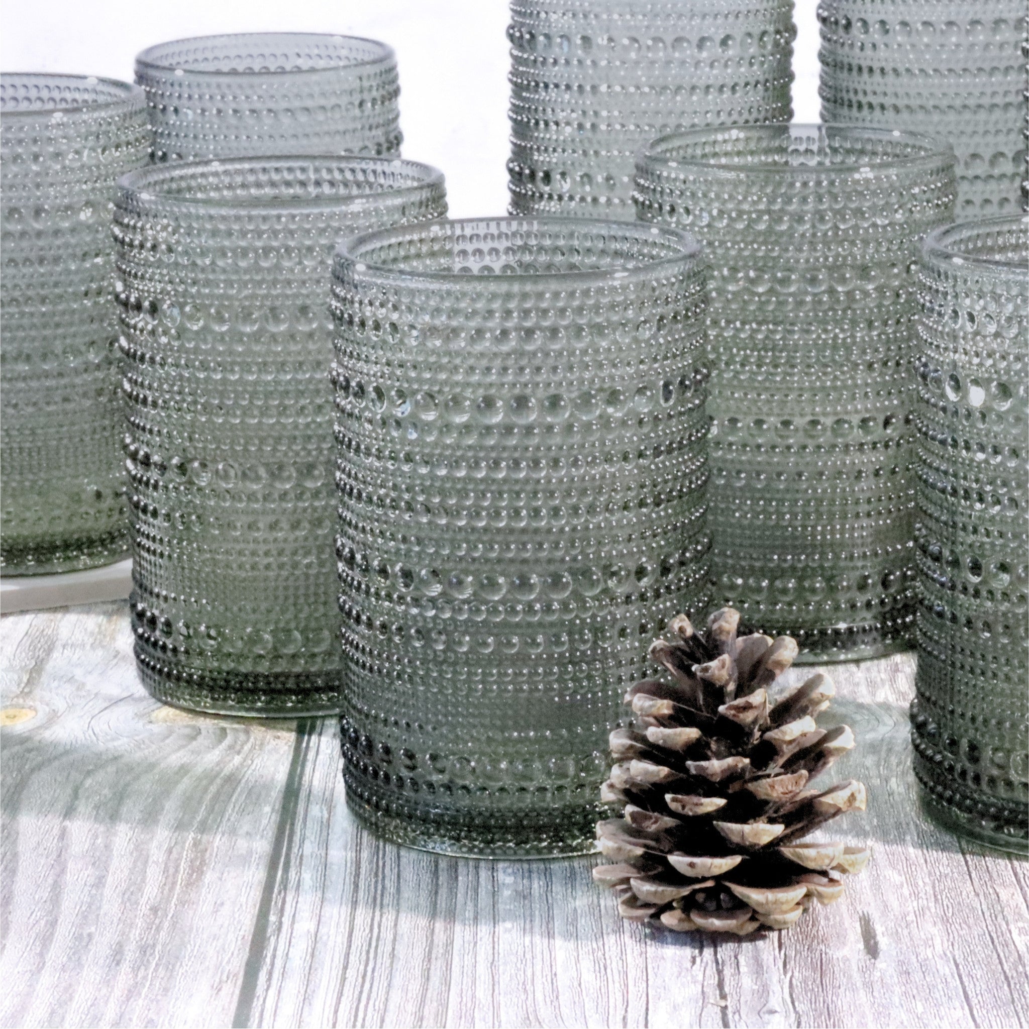 Grey hobnail bead glasses with a pine cone on a wooden surface