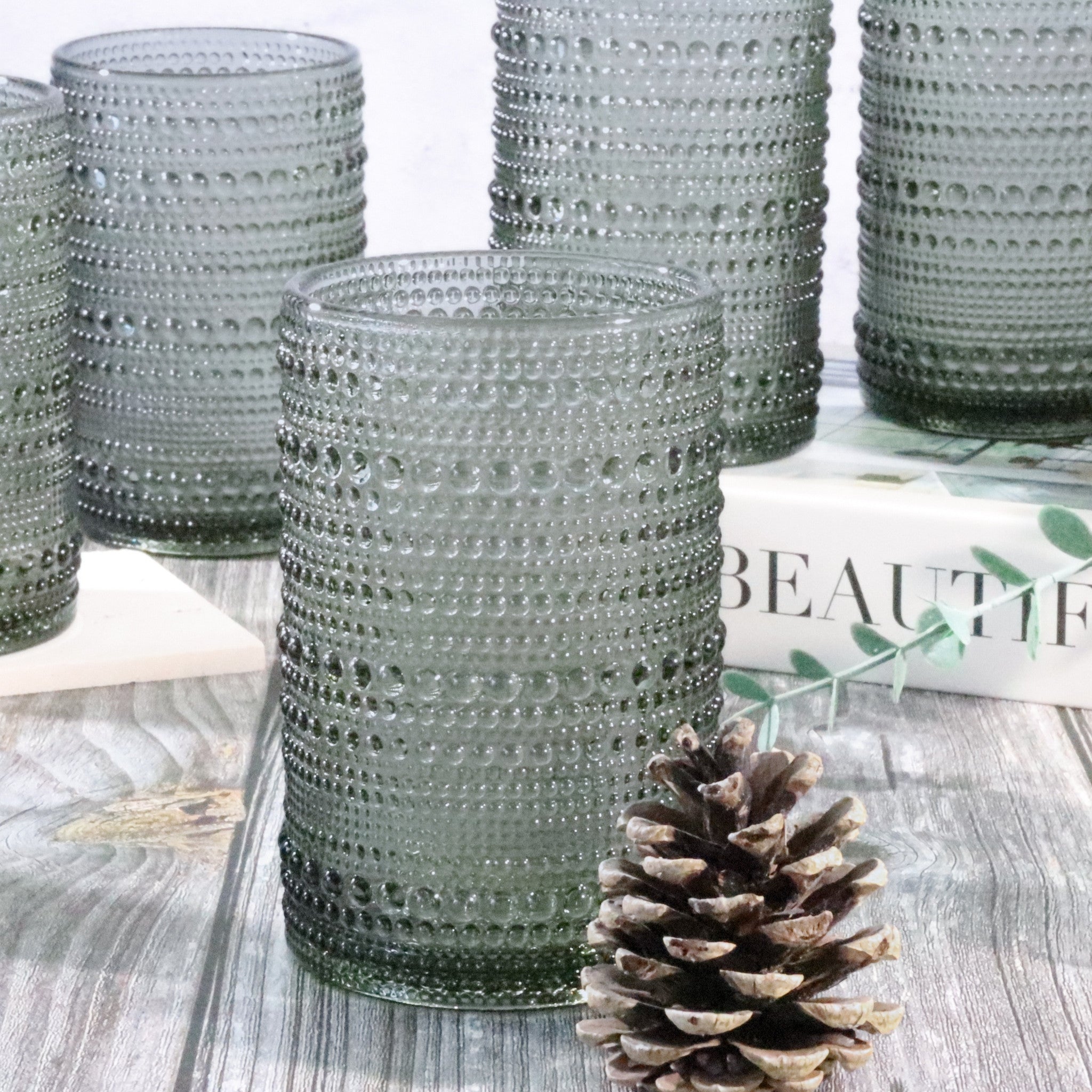 Set of grey textured hobnail bead tumblers on a wooden surface with a pine cone and magazine.