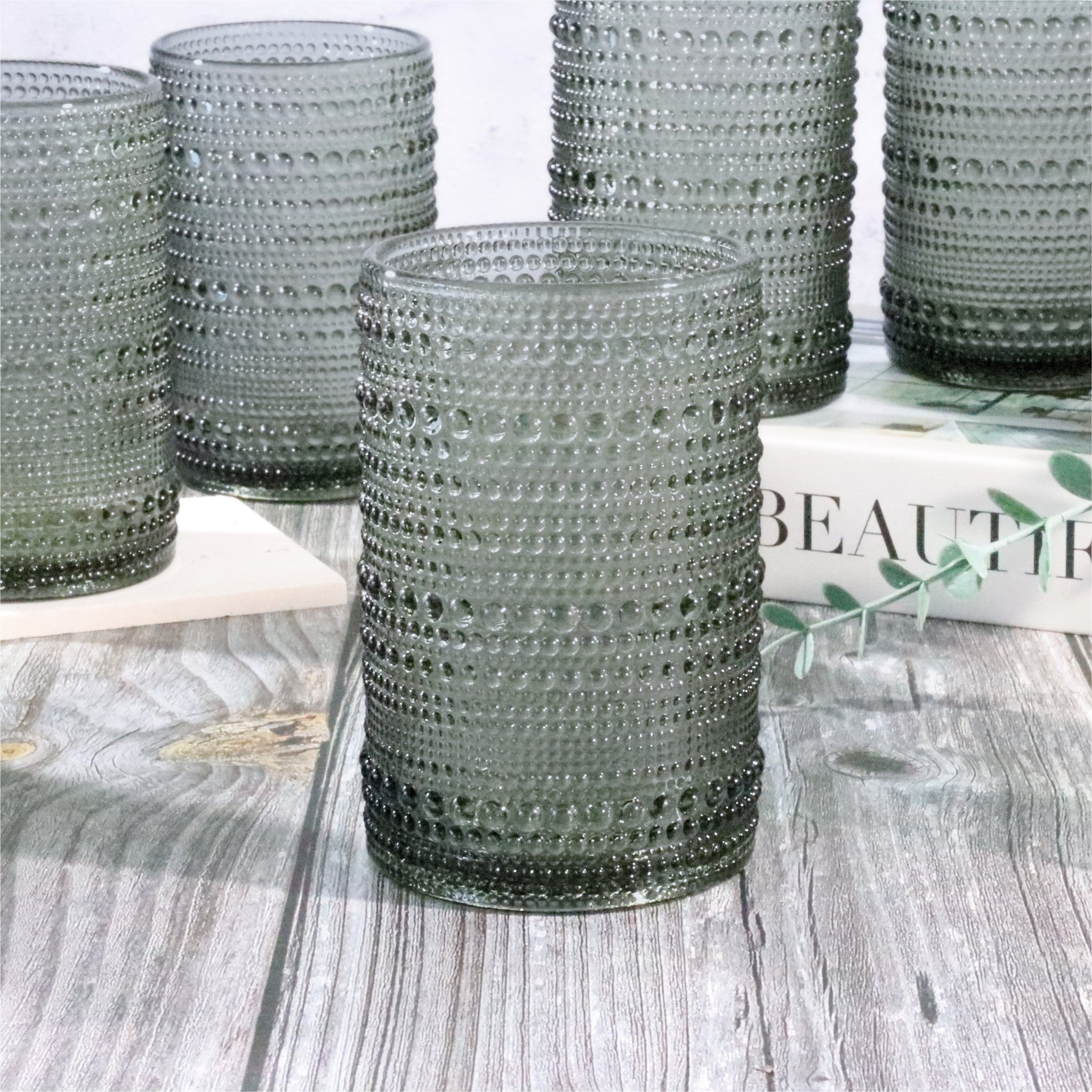 Set of hobnail bead grey tumblers on a wooden surface with a magazine in the background.