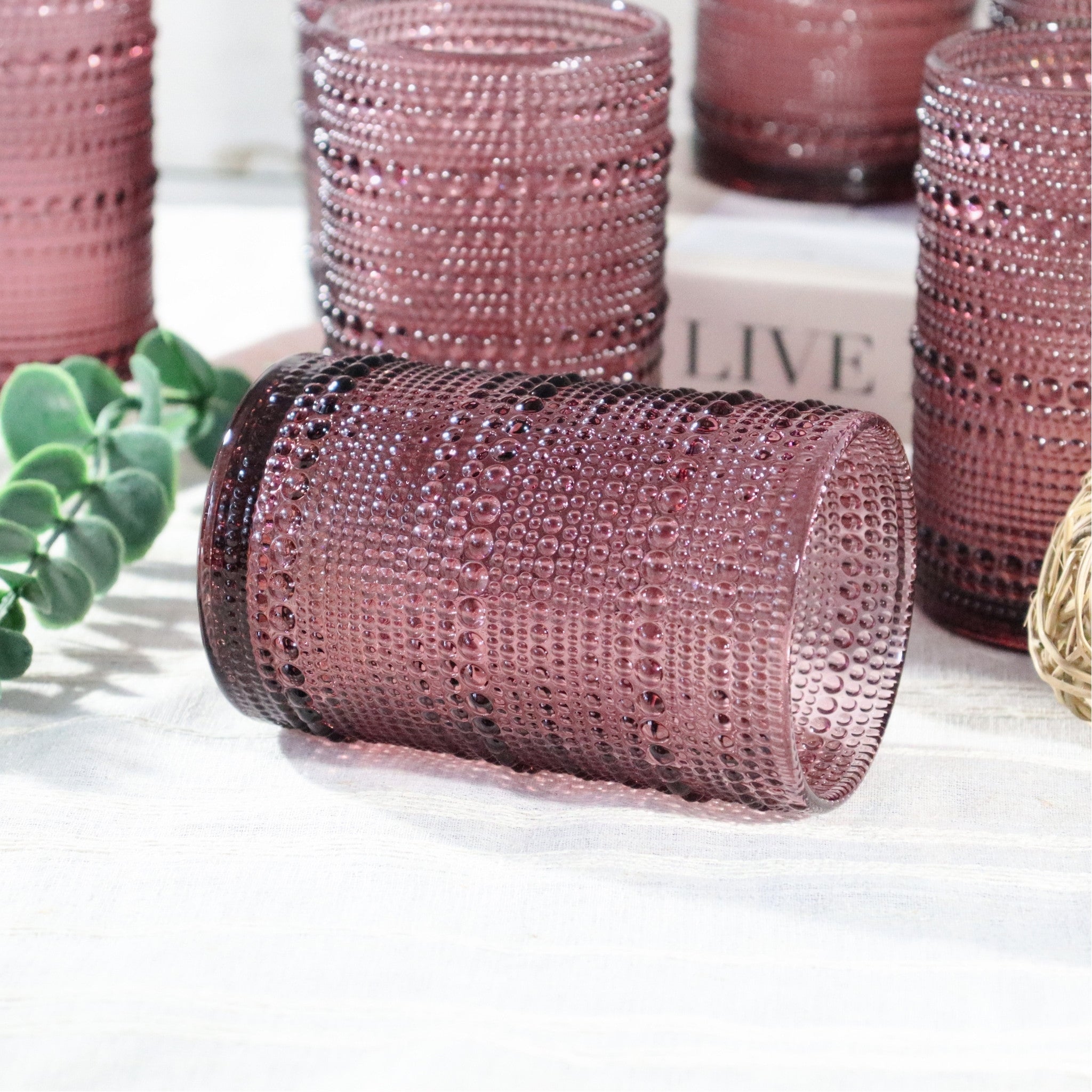 Decorative purple glass tumblers on a white surface with greenery and a book in the background.