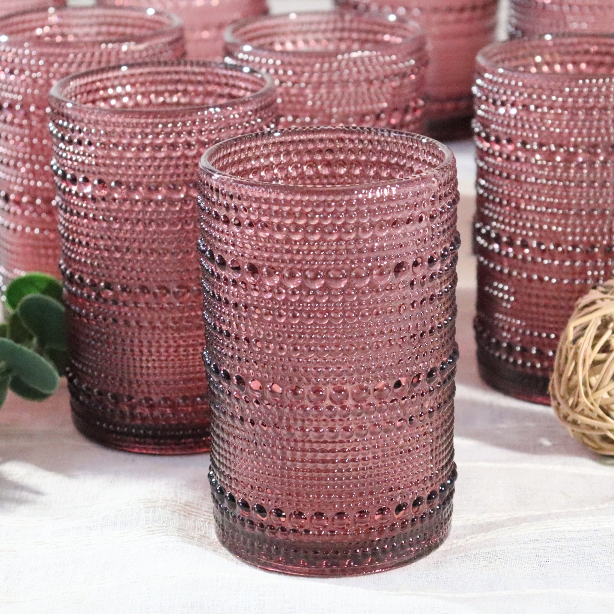 Pink beaded glasses on a white surface with a plant and decorative ball in the background