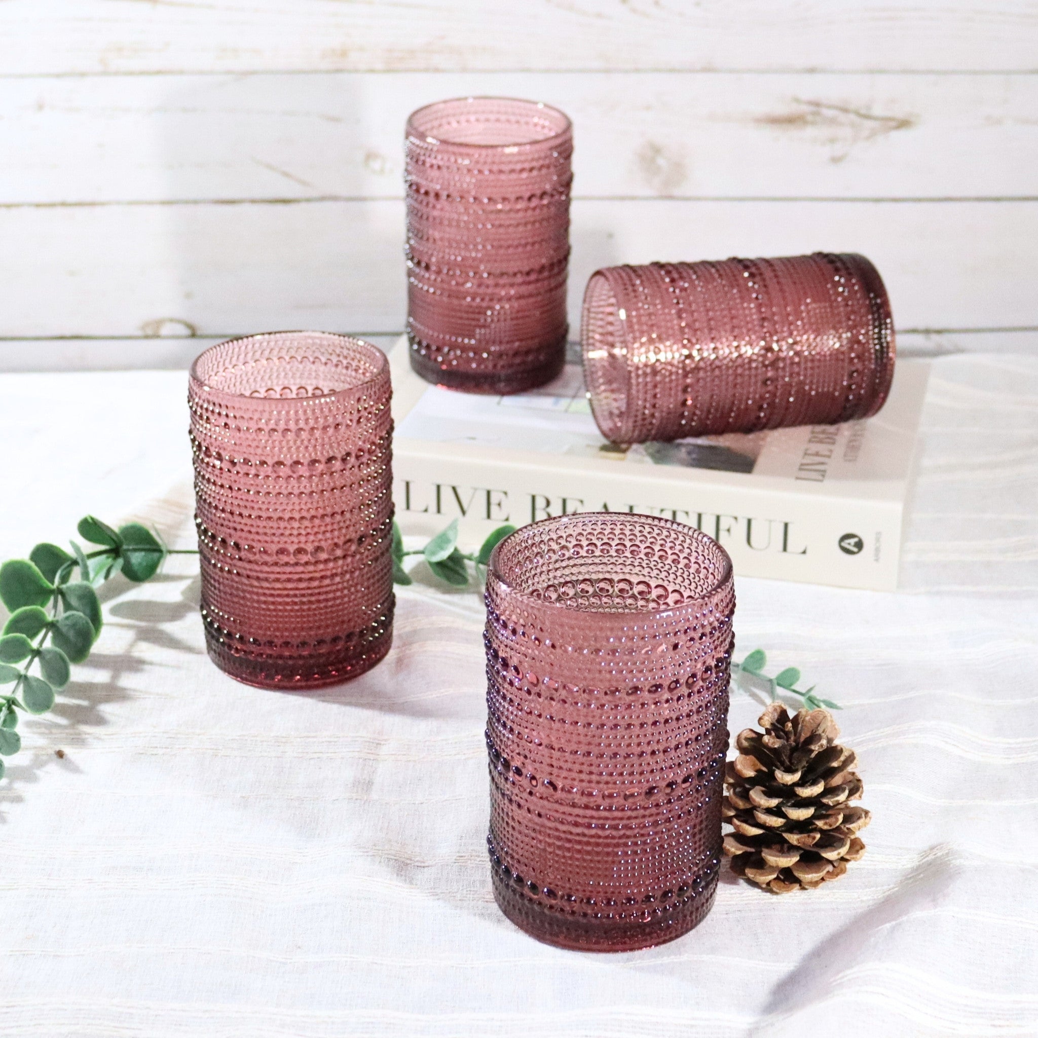 Set of four purple textured glass tumblers on a white surface with a wooden background.