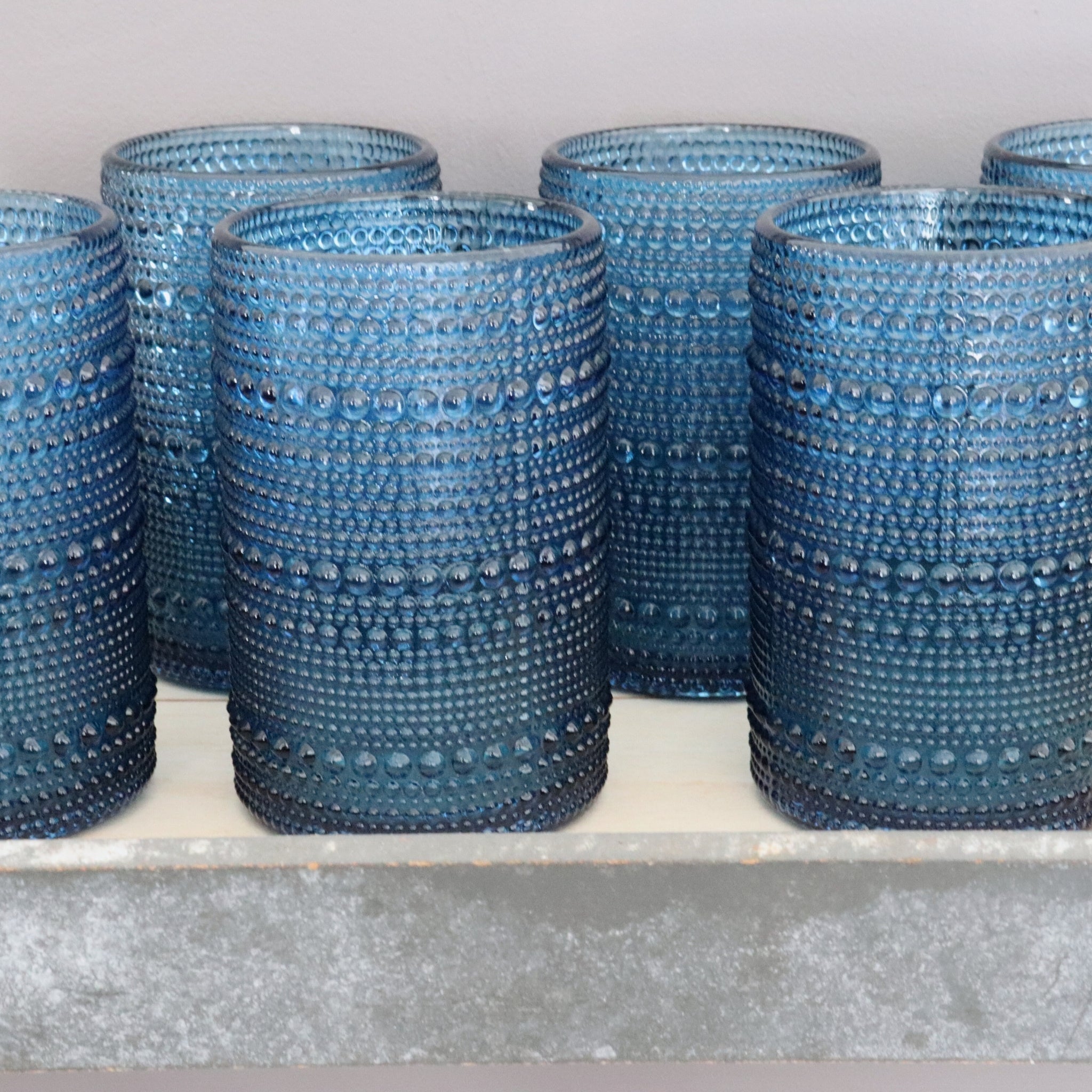 Set of blue hobnail glassware on a white surface with a light grey background