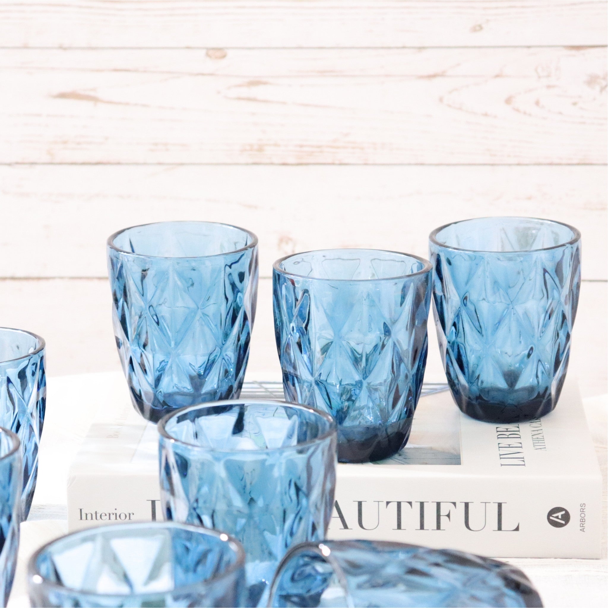 Set of blue glass tumblers on a wooden surface with a magazine underneath.