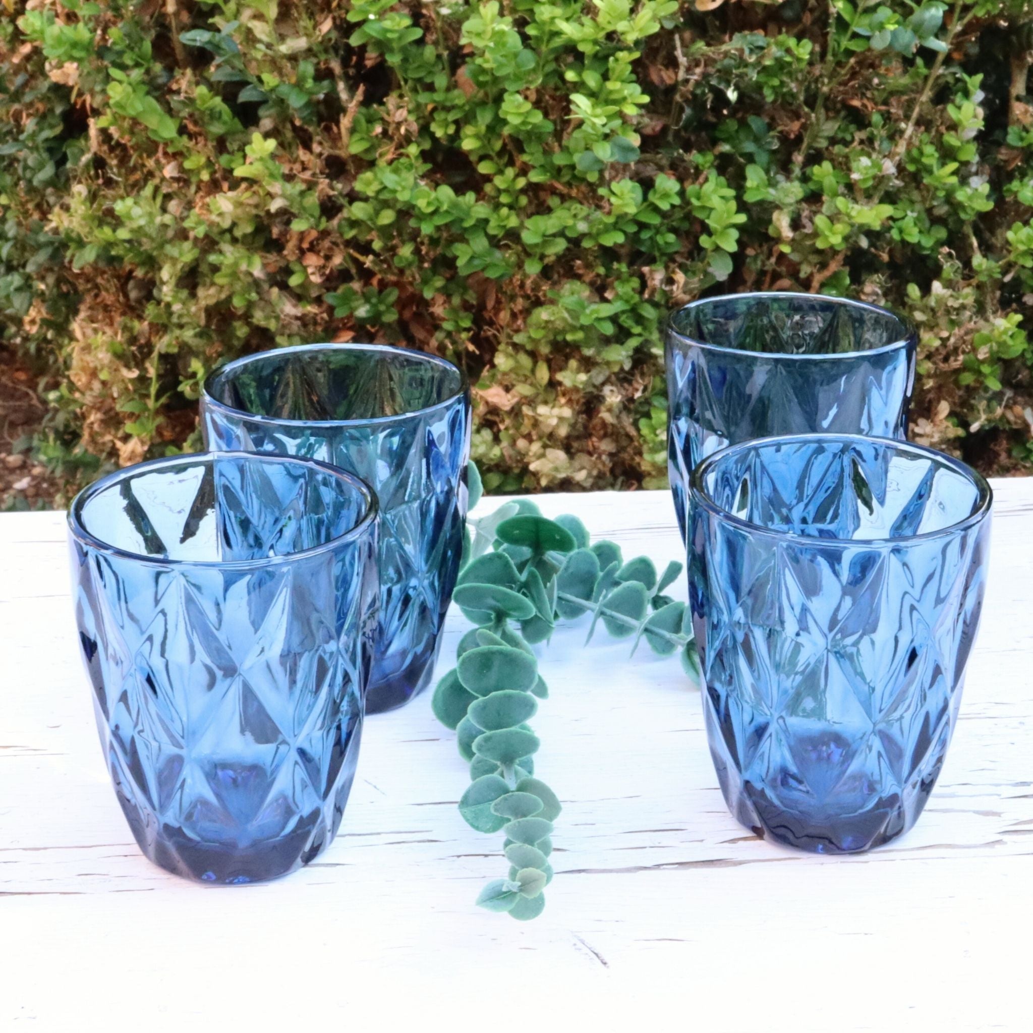 Set of blue glass tumblers on a wooden surface with greenery in the background