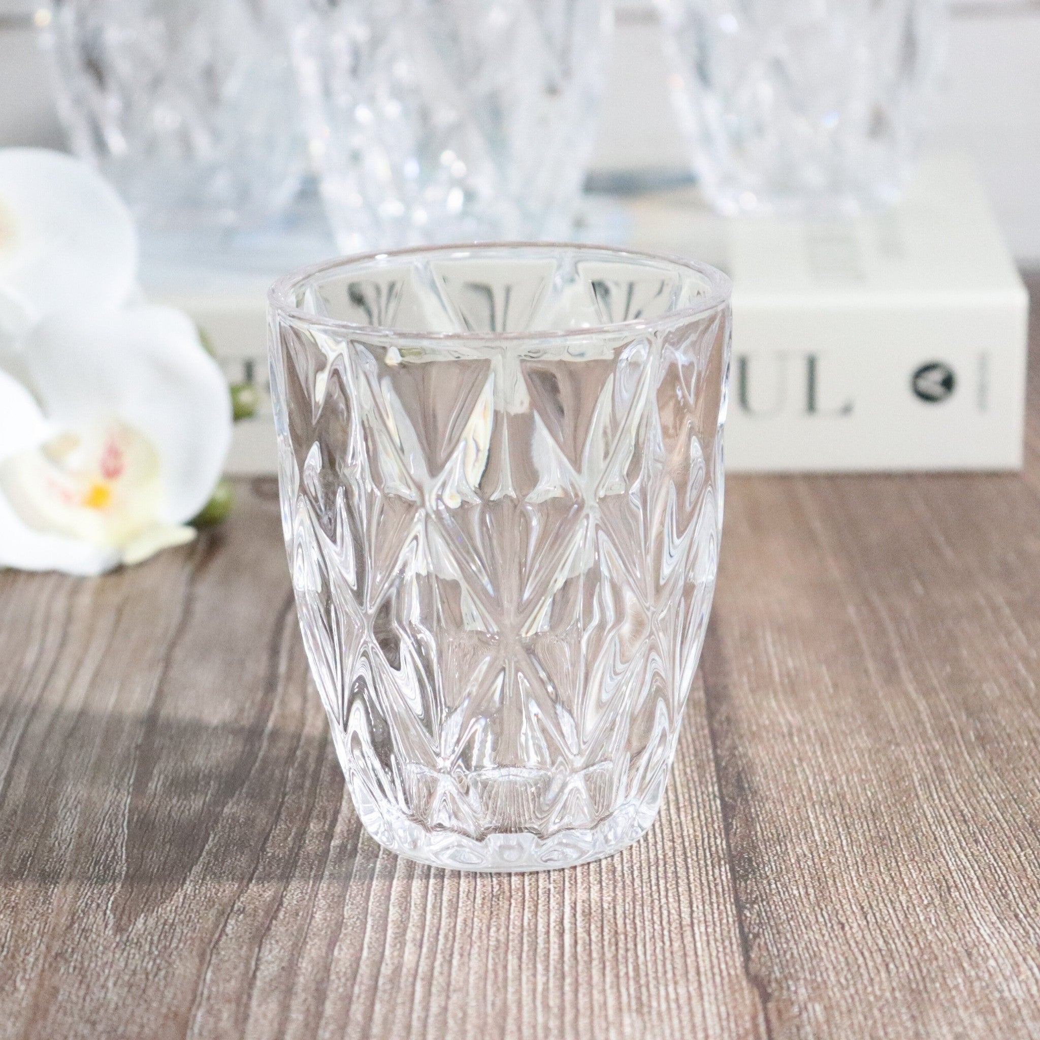 Clear glass tumbler with diamond pattern on a wooden surface with blurred background