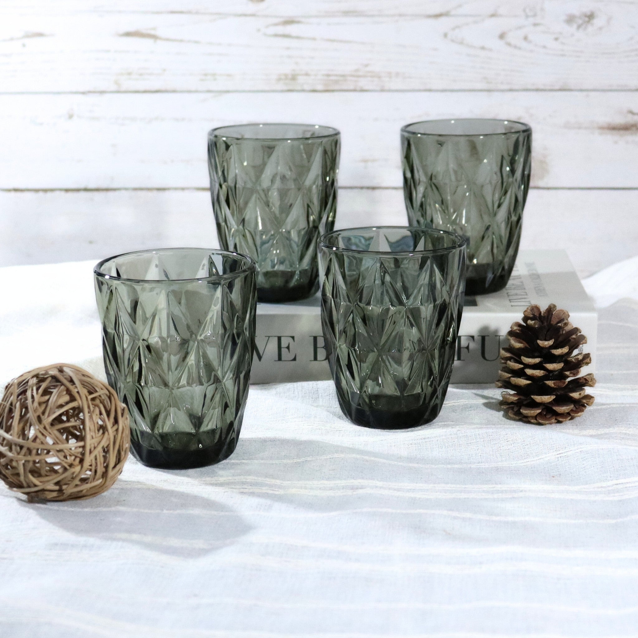 Set of four textured green glass tumblers on a white surface with decorative elements.