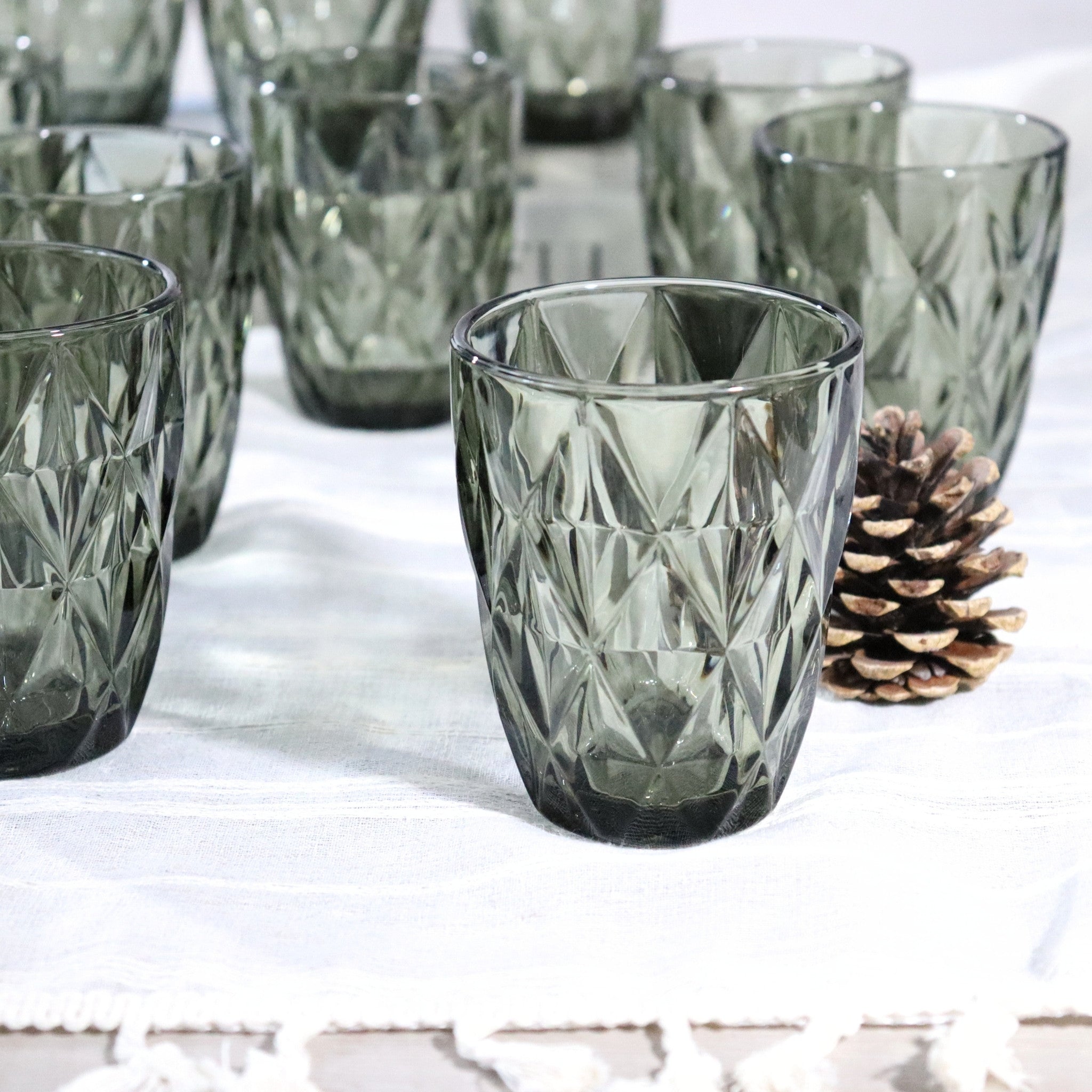 Set of diamond-cut glass tumblers on a white surface with a pine cone.