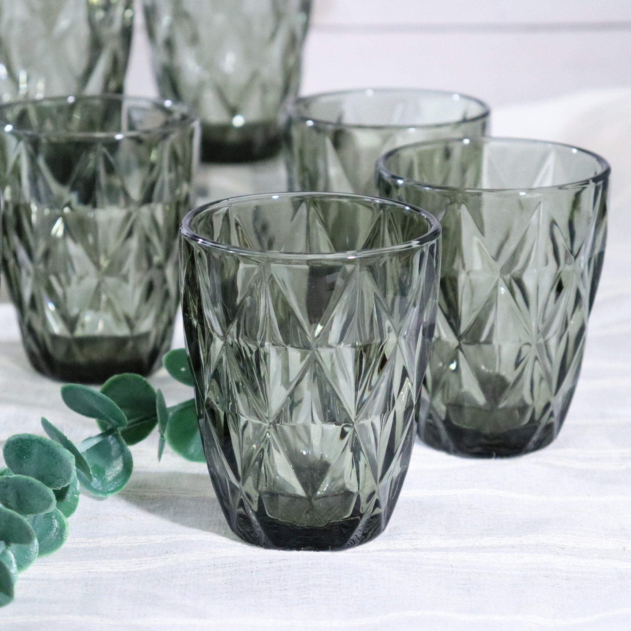Set of diamond-cut glass tumblers on a white surface with greenery.