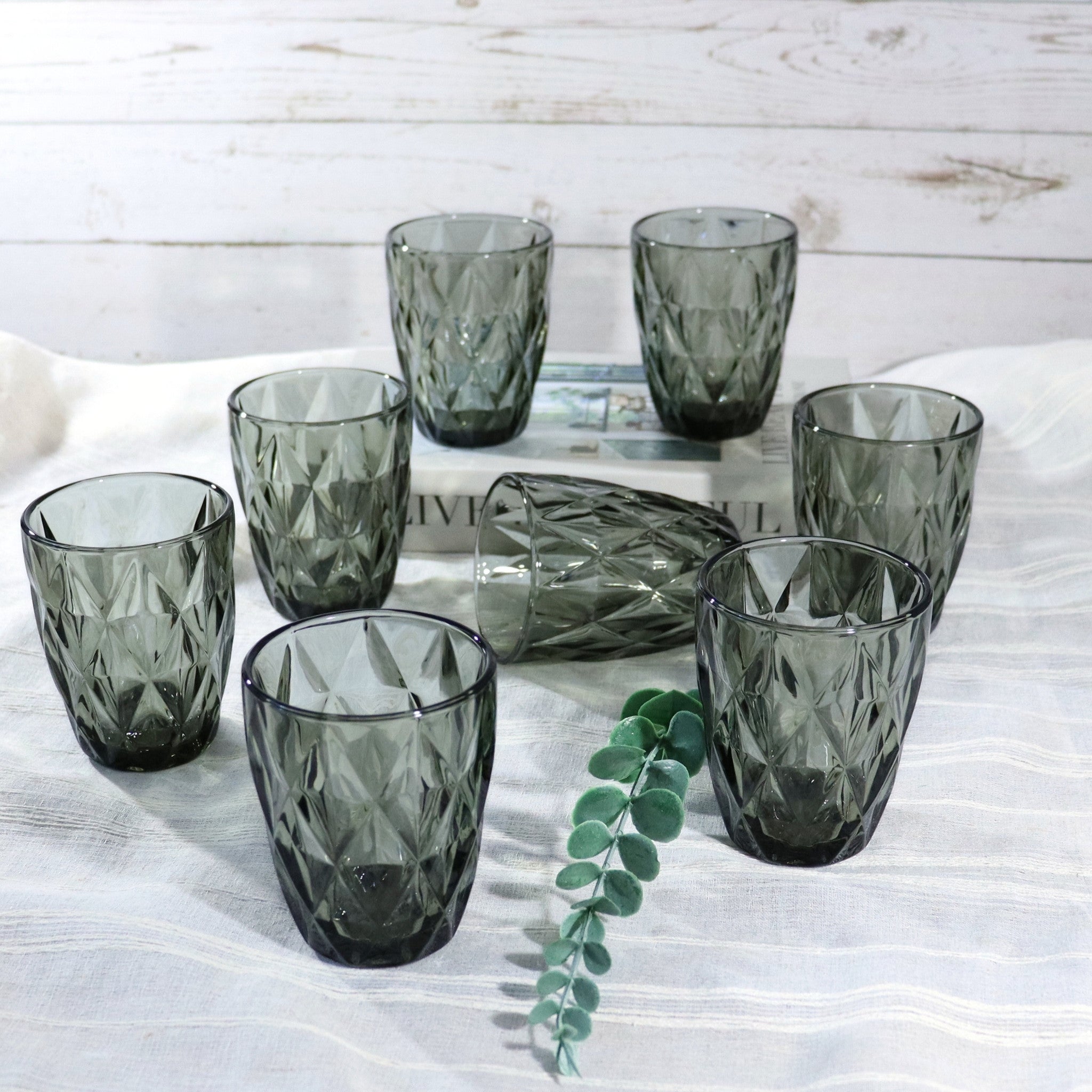 Set of dark green glass tumblers on a white surface with a wooden background