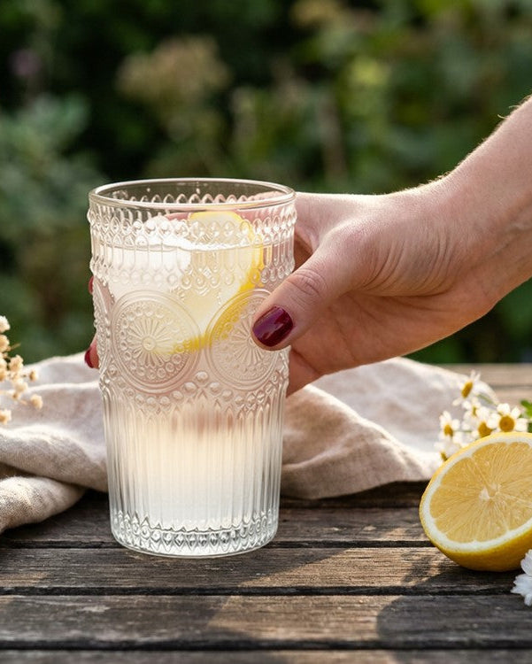 Set of clear glass tumblers with embossed designs on a wooden surface against a gray wall.