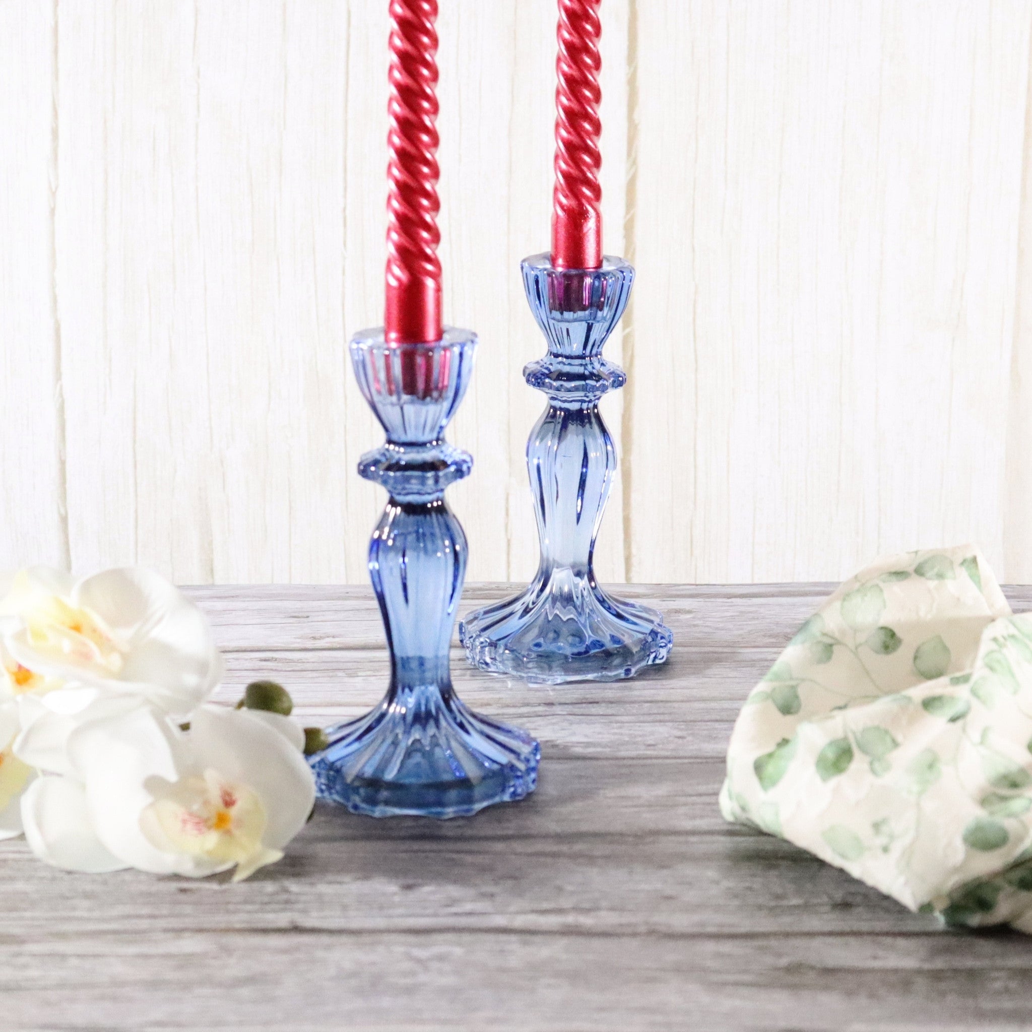 Blue glass candlestick holders with red candles on a wooden surface.