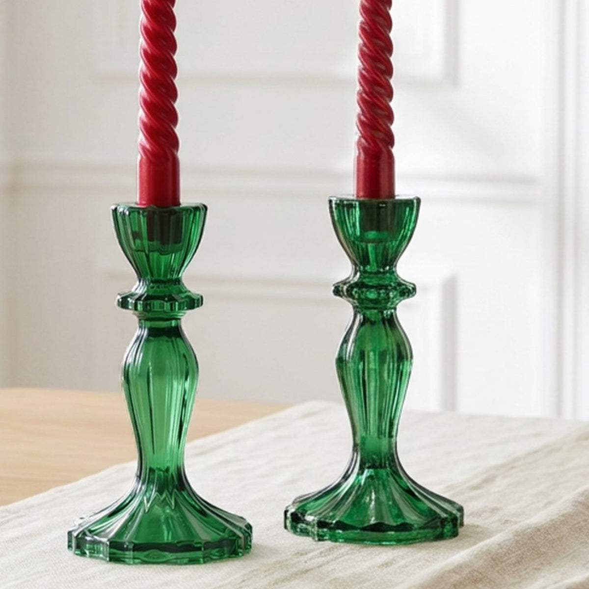 Two red spiral candles in green candlesticks on a wooden surface with white flowers.